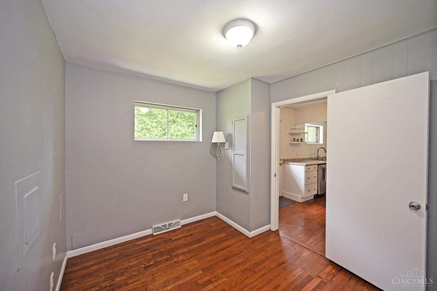 Unfurnished room with hardwood floors, a high window, and an open doorway to the kitchen.