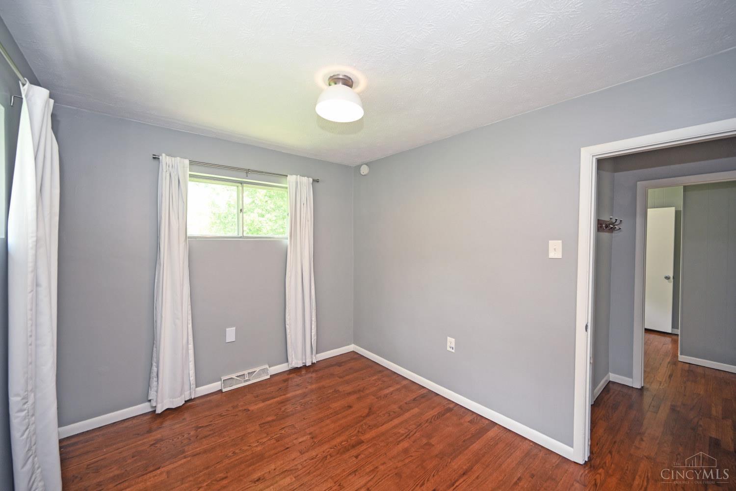 Empty gray room with hardwood floors, a curtained window, and an open doorway.