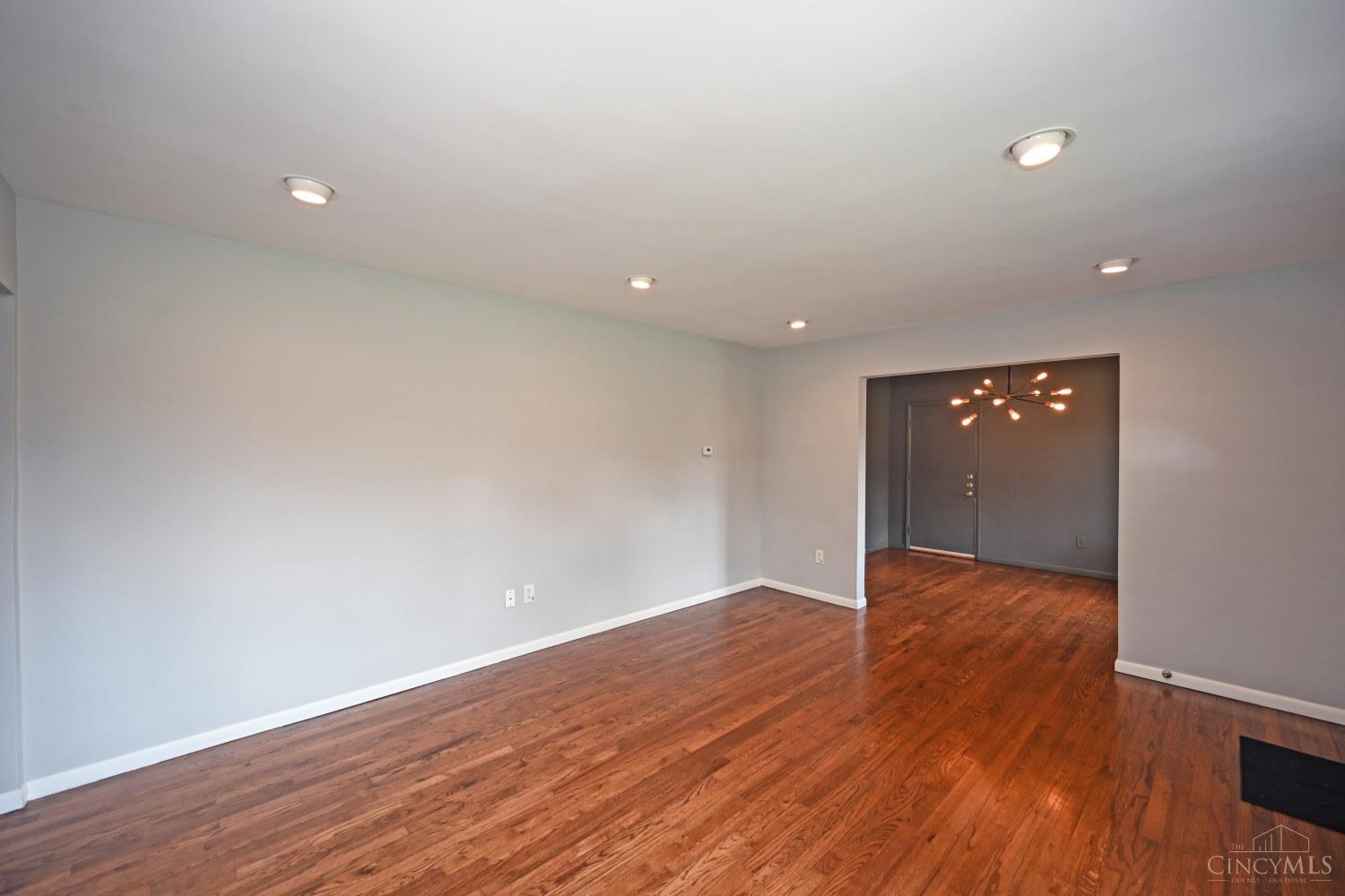 Empty room with hardwood floors and a wide opening to the front entry.