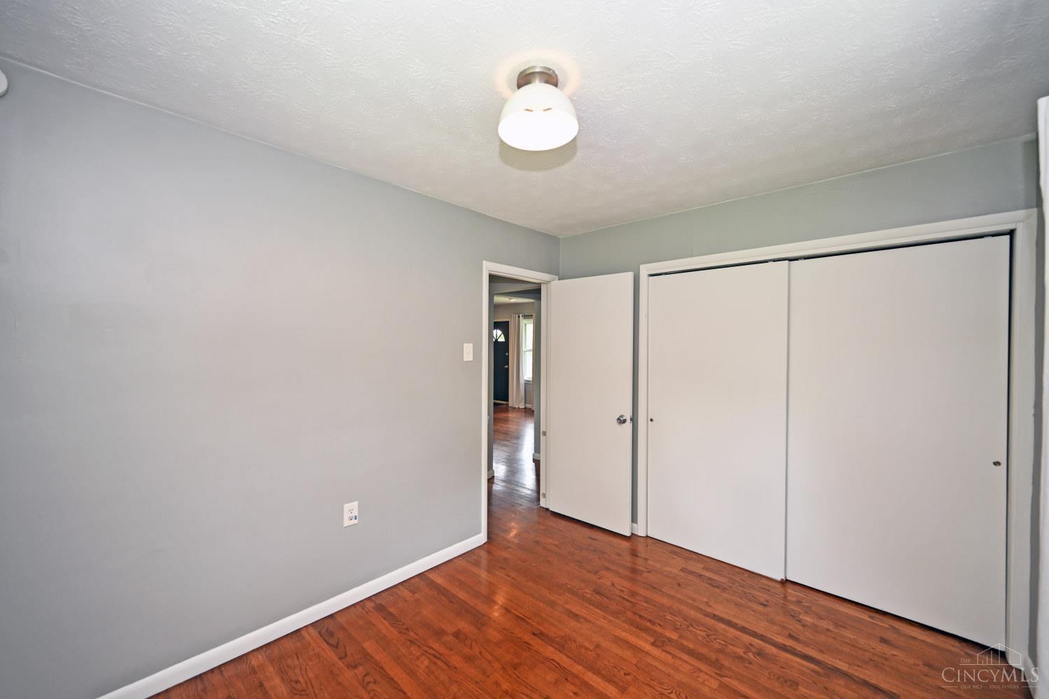 Empty bedroom with reddish hardwood floors, gray walls, and a large white sliding-door closet.