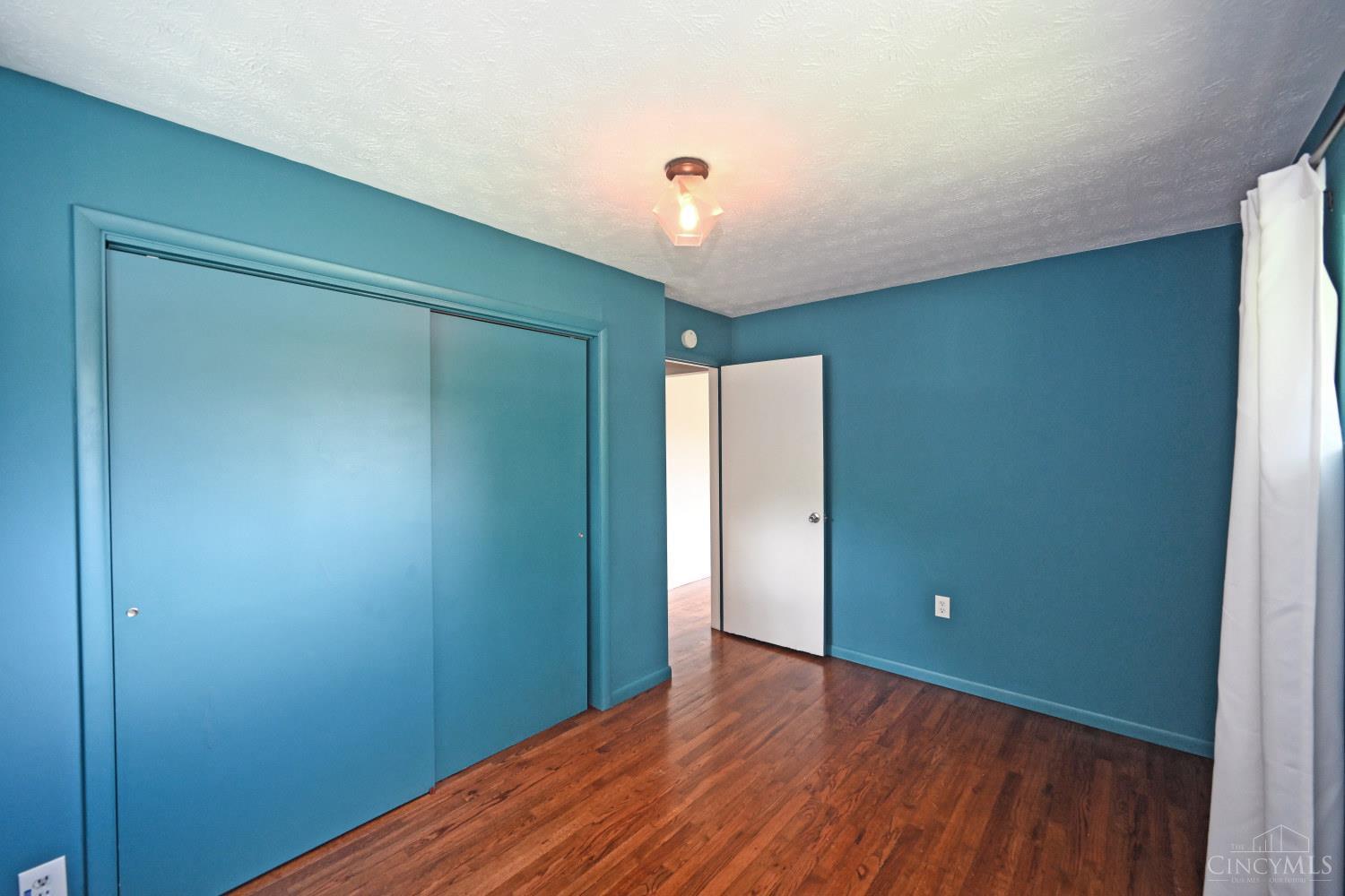 Empty bedroom with teal walls, hardwood floors, and a large sliding closet door.