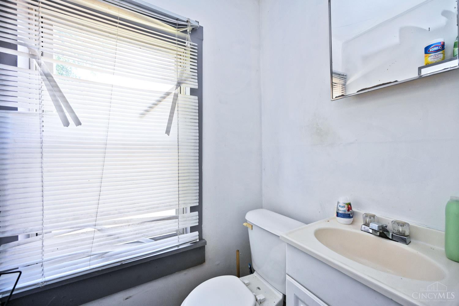 Bathroom with a white toilet and vanity beside a large window with horizontal blinds.