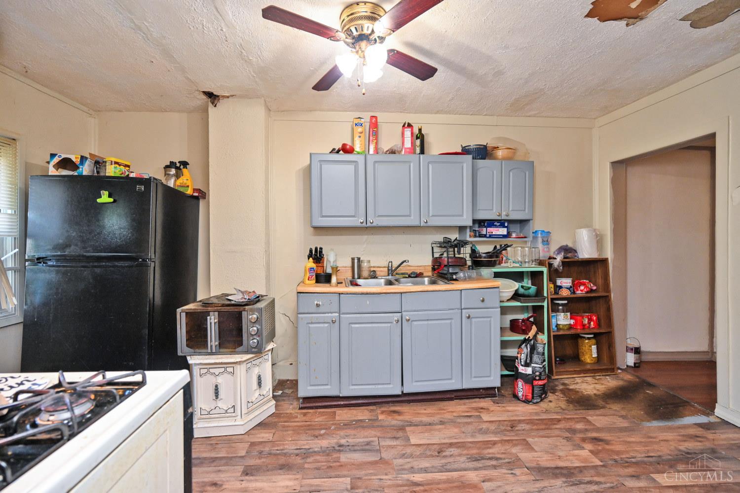 Kitchen with gray-blue cabinets, a black refrigerator, and a damaged ceiling.