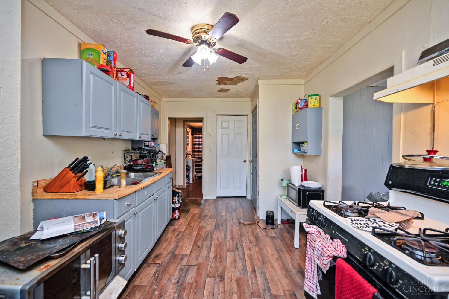 Narrow kitchen with blue-gray cabinets, a gas stove, and damaged ceiling plaster.