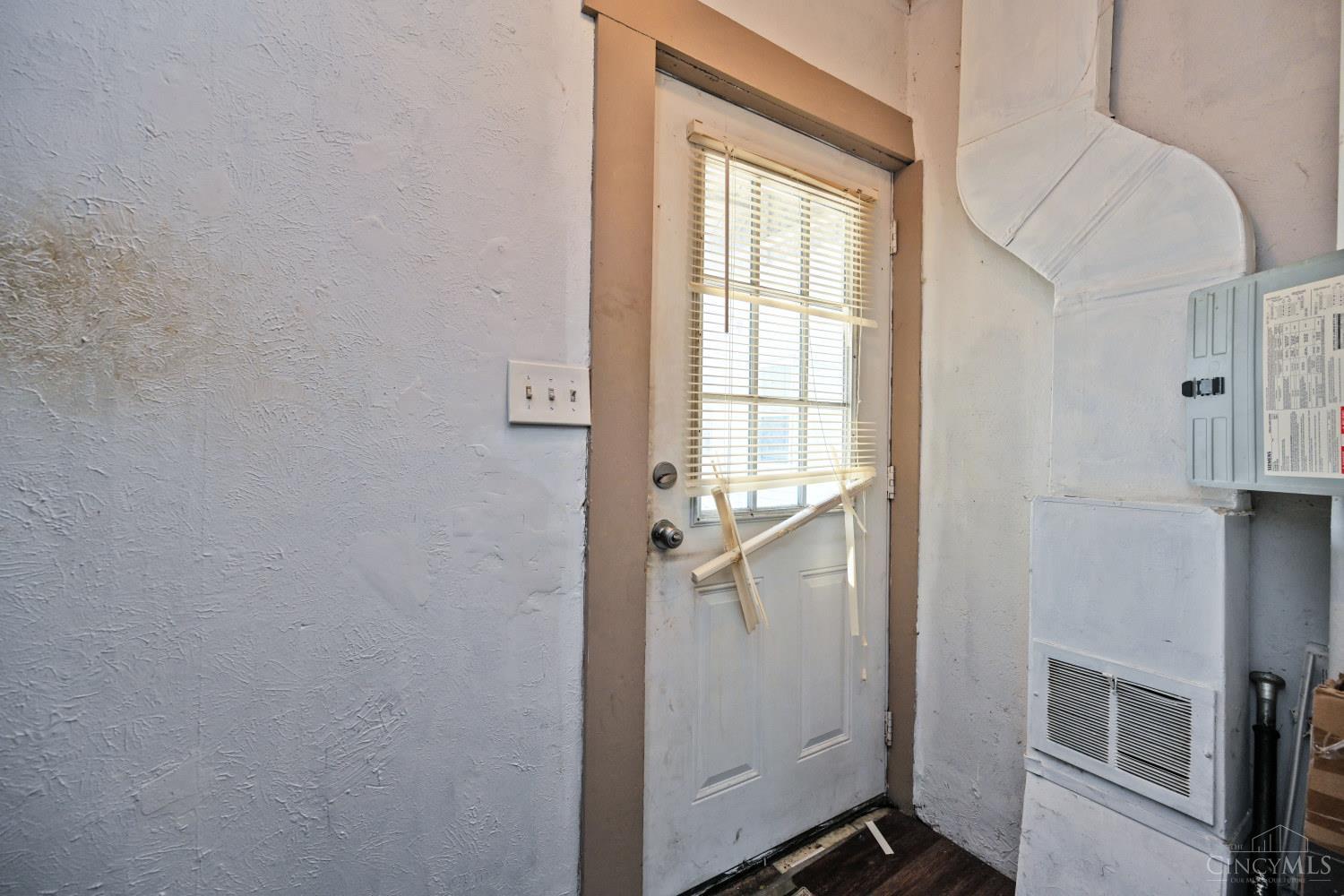 Utility area with a door, exposed ductwork, electrical panel, and wall vent.
