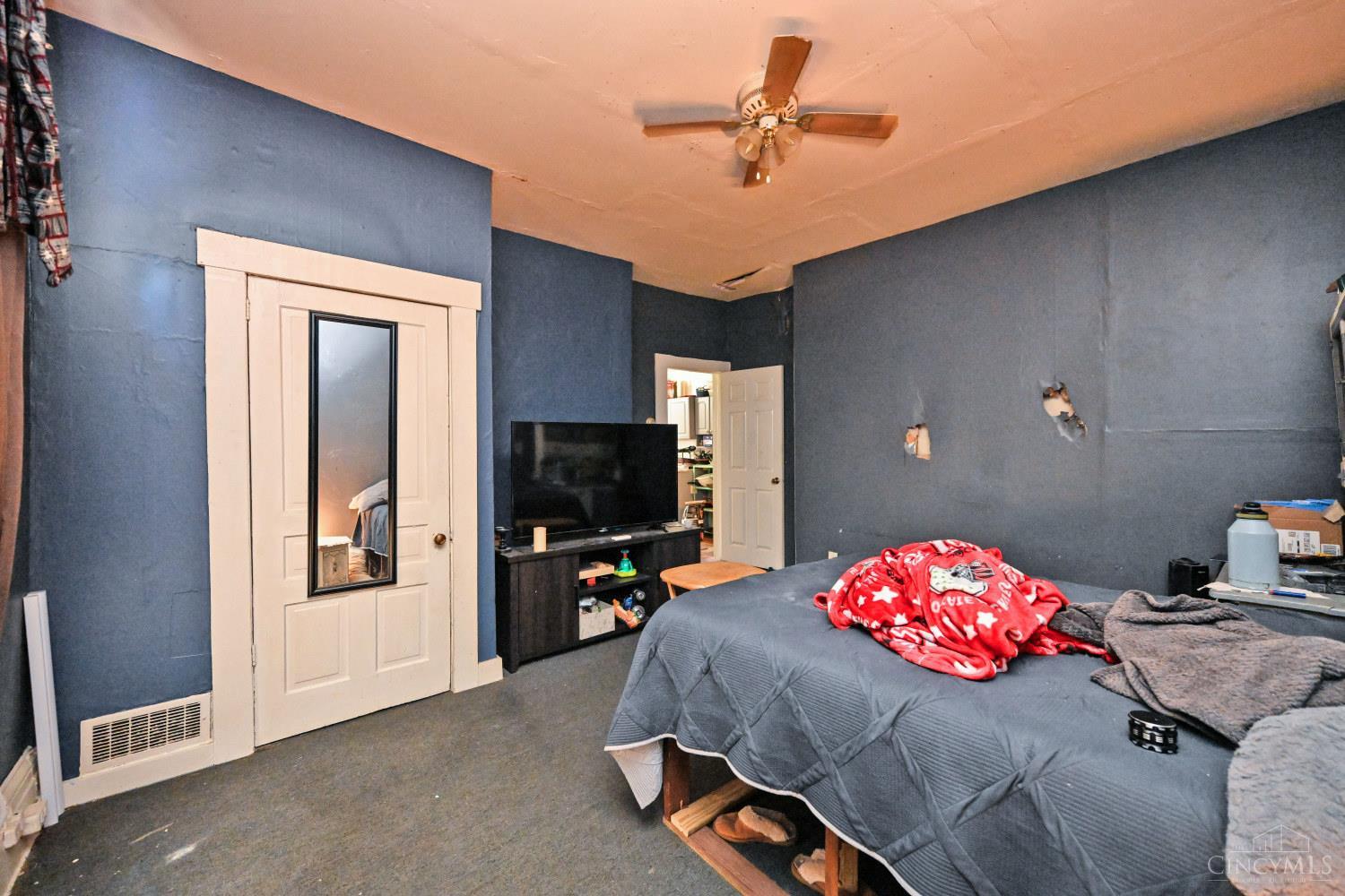 Bedroom with dark blue walls, a gray bed, mirrored closet door, and ceiling fan.
