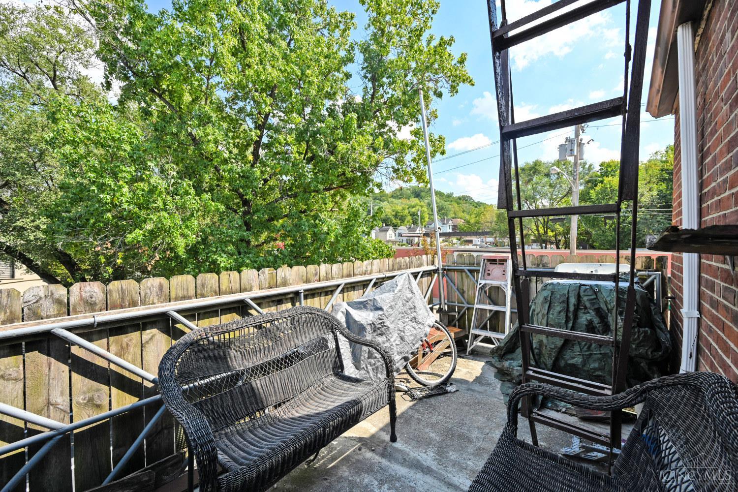 Outdoor deck with black wicker seating, a wooden privacy fence, and leafy trees.