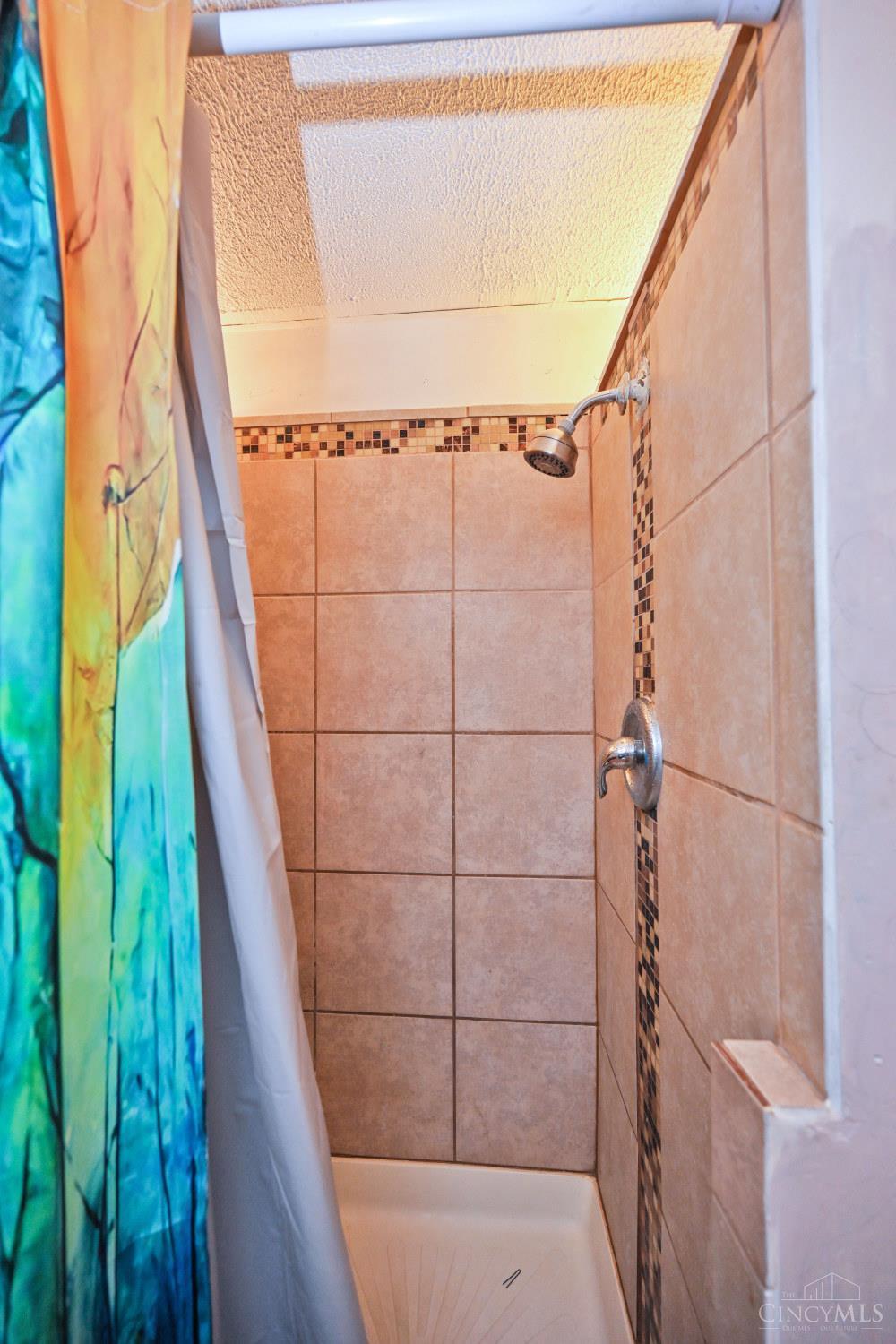 Tiled shower with a blue-green patterned curtain and mosaic accent strip.