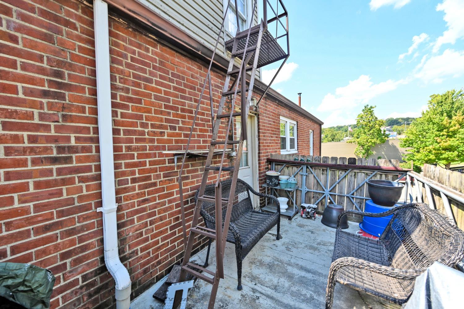 Brick-walled patio with wicker seating, planters, and a metal exterior staircase.
