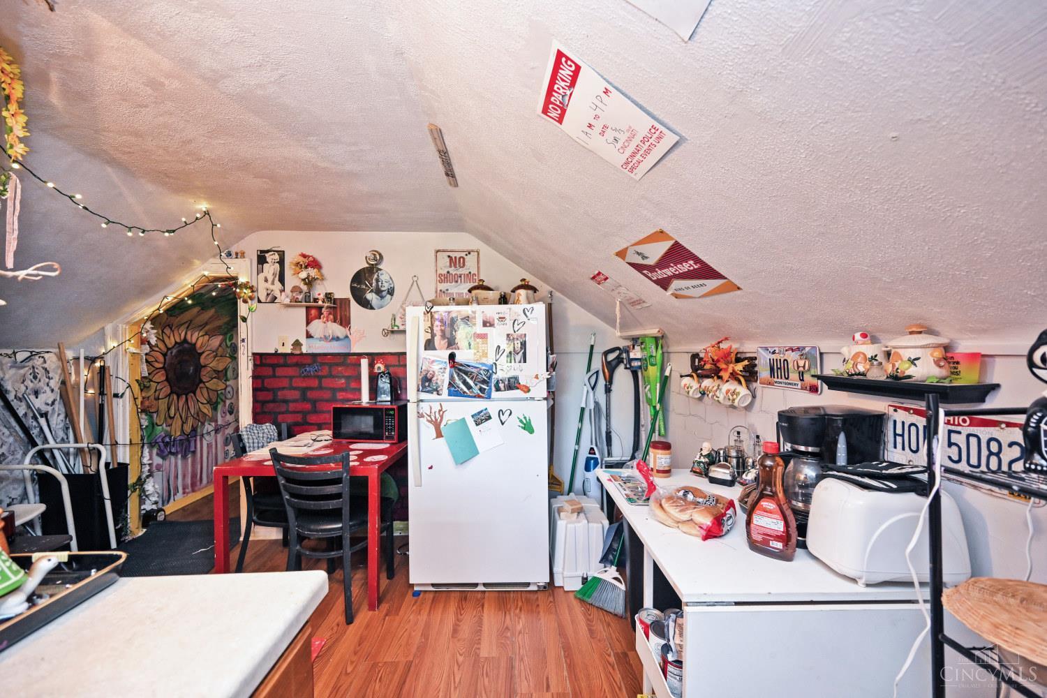 Crowded kitchen beneath a sloped ceiling, with a photo-covered refrigerator and red dining table.