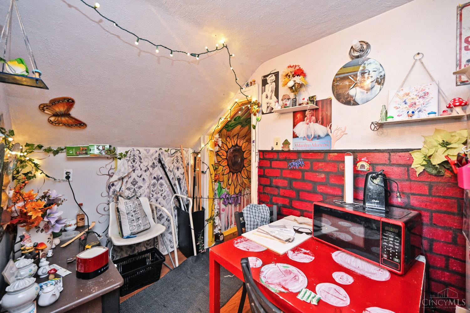 Eclectic dining area with a red table, microwave, and red brick hearth beneath a sloped ceiling.