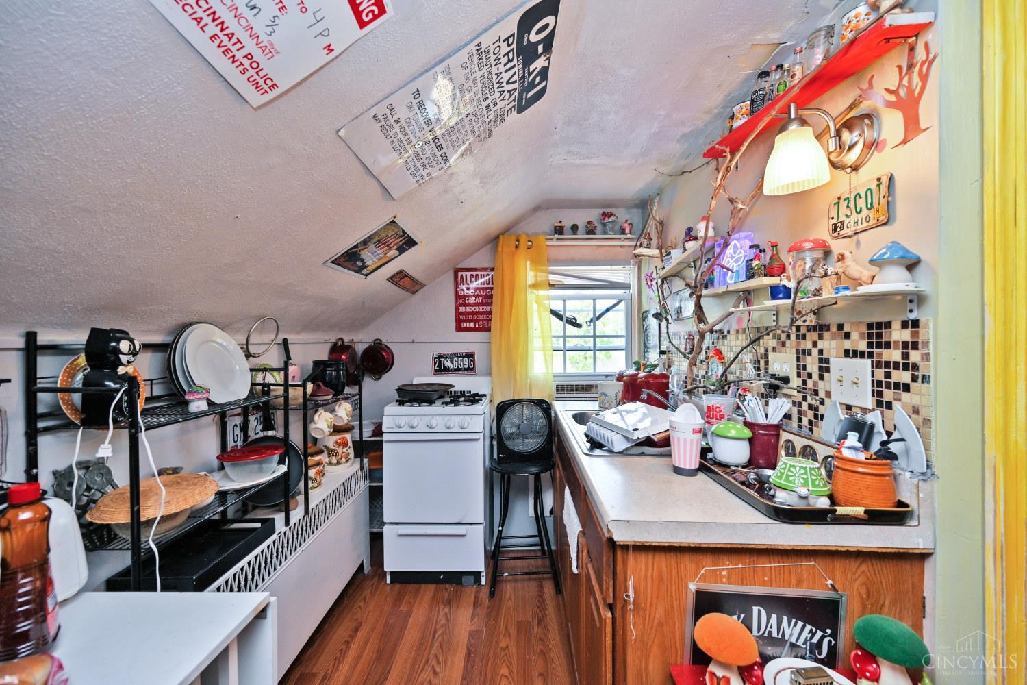 Cluttered kitchen with a sloped ceiling, white stove, crowded shelves, and a long counter.