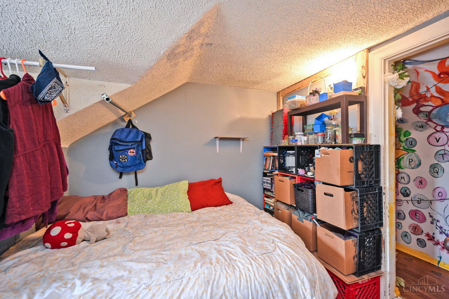 Bedroom with a sloped ceiling, a bed, storage shelves, and a brightly painted door.