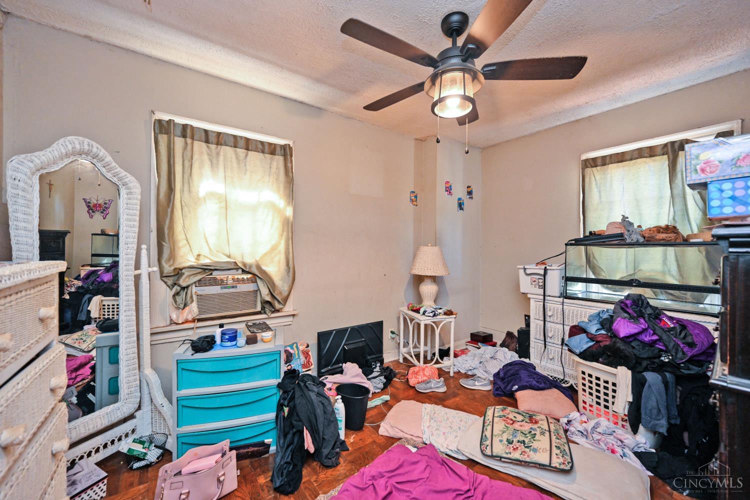 Cluttered bedroom with an aquarium, ceiling fan, and clothes scattered across the floor.