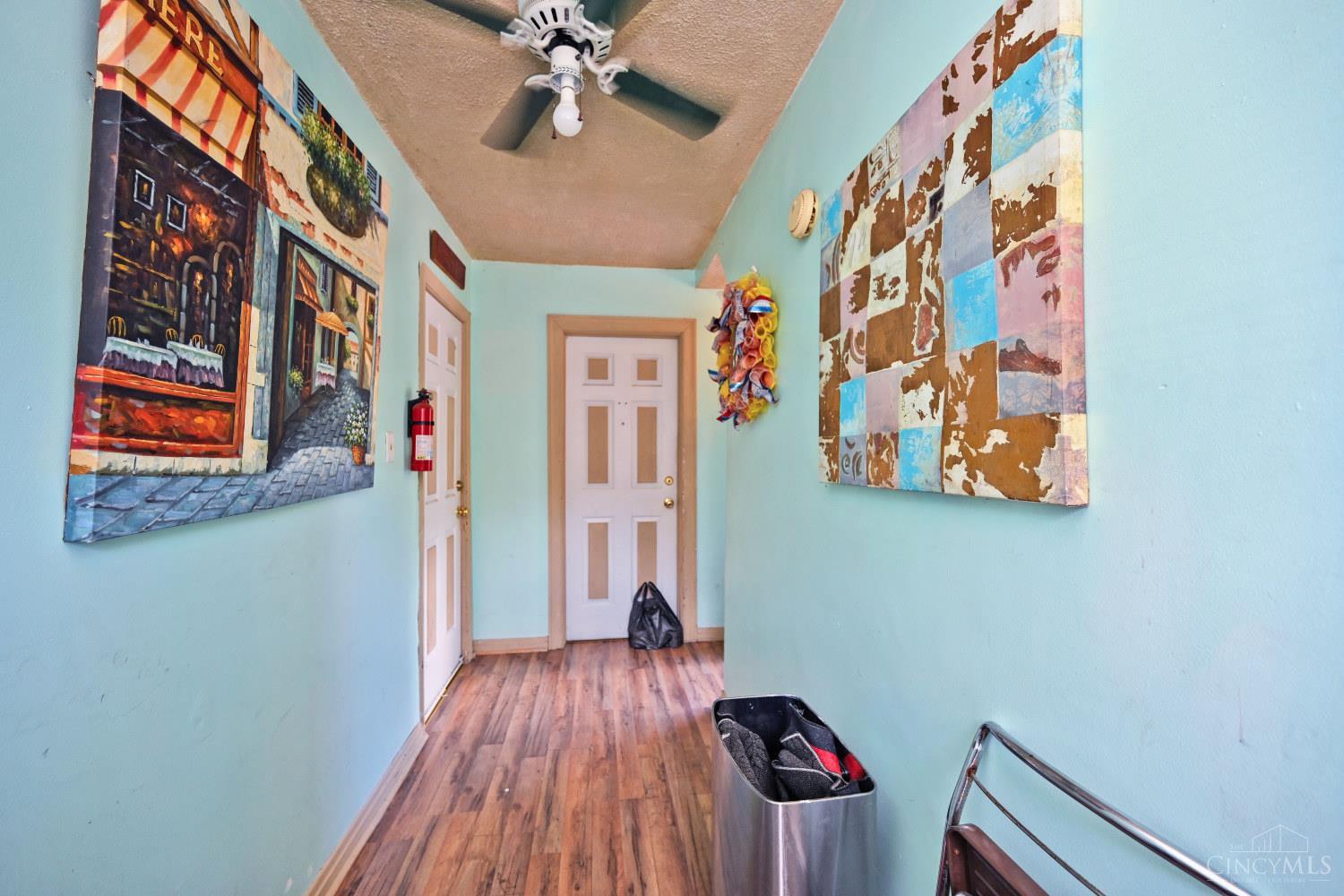 Narrow aqua hallway with wood-look flooring, colorful wall art, white doors, and a ceiling fan.