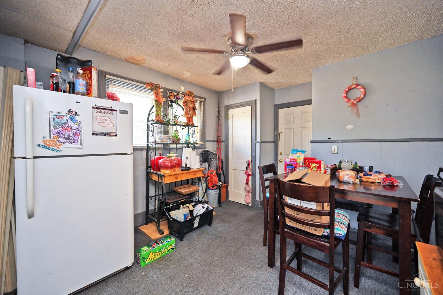 Kitchen and dining area with a white refrigerator, crowded table, and ceiling stains.