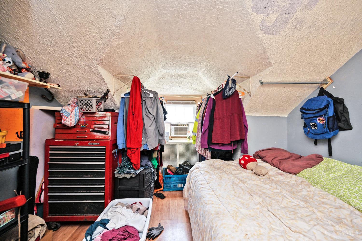 Bedroom with a bed, hanging clothes, red tool chest, and low sloped ceiling.