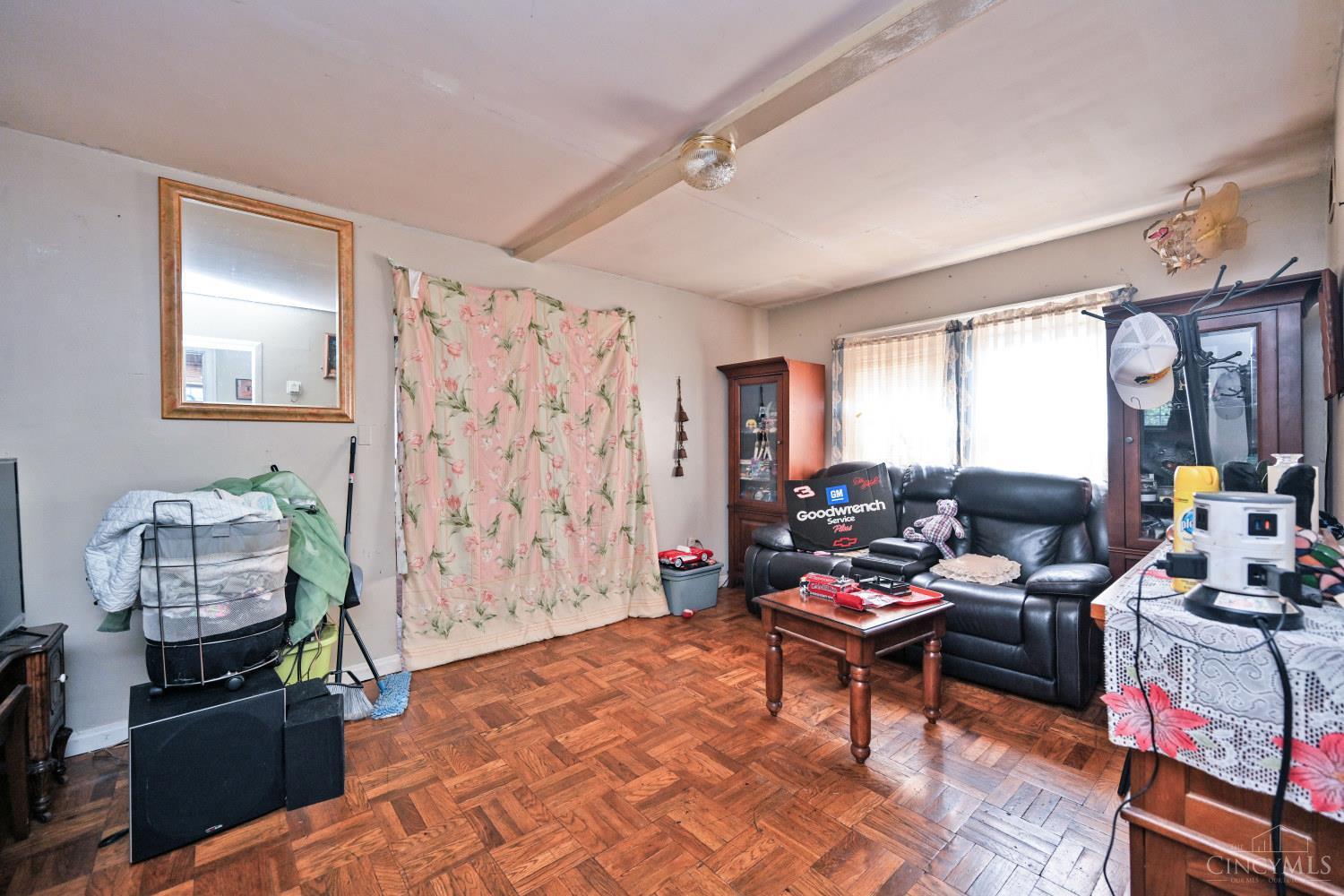 Living room with parquet flooring, a black leather sofa, floral curtains, and glass-front cabinets.