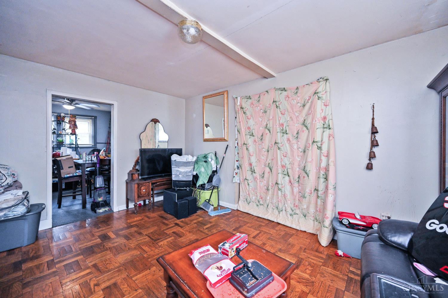Living room with parquet flooring, floral curtains, and a television beside an adjoining room.