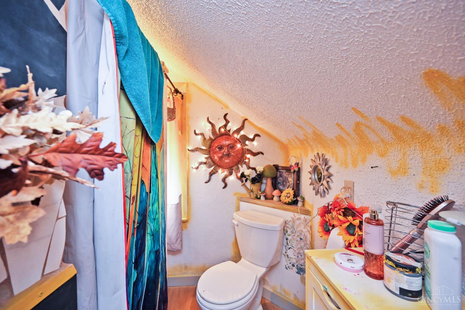 Bathroom with a low sloped ceiling, colorful shower curtain, sun decorations, and crowded vanity.