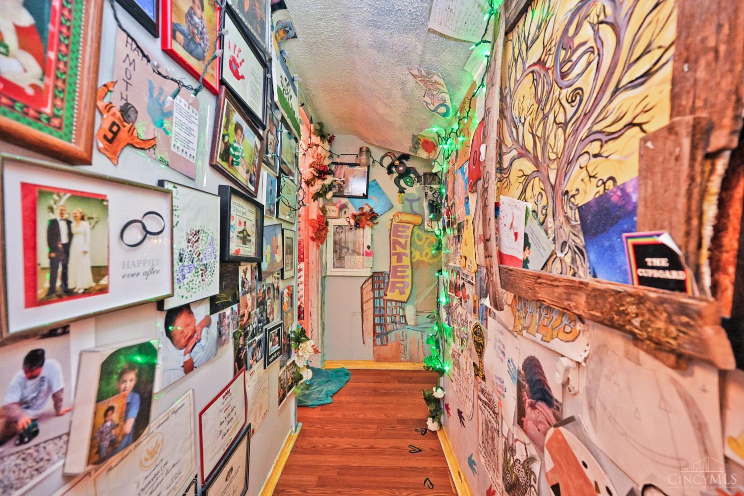 Eclectic hallway lined with framed photos and artwork, with green string lights and hardwood floors.