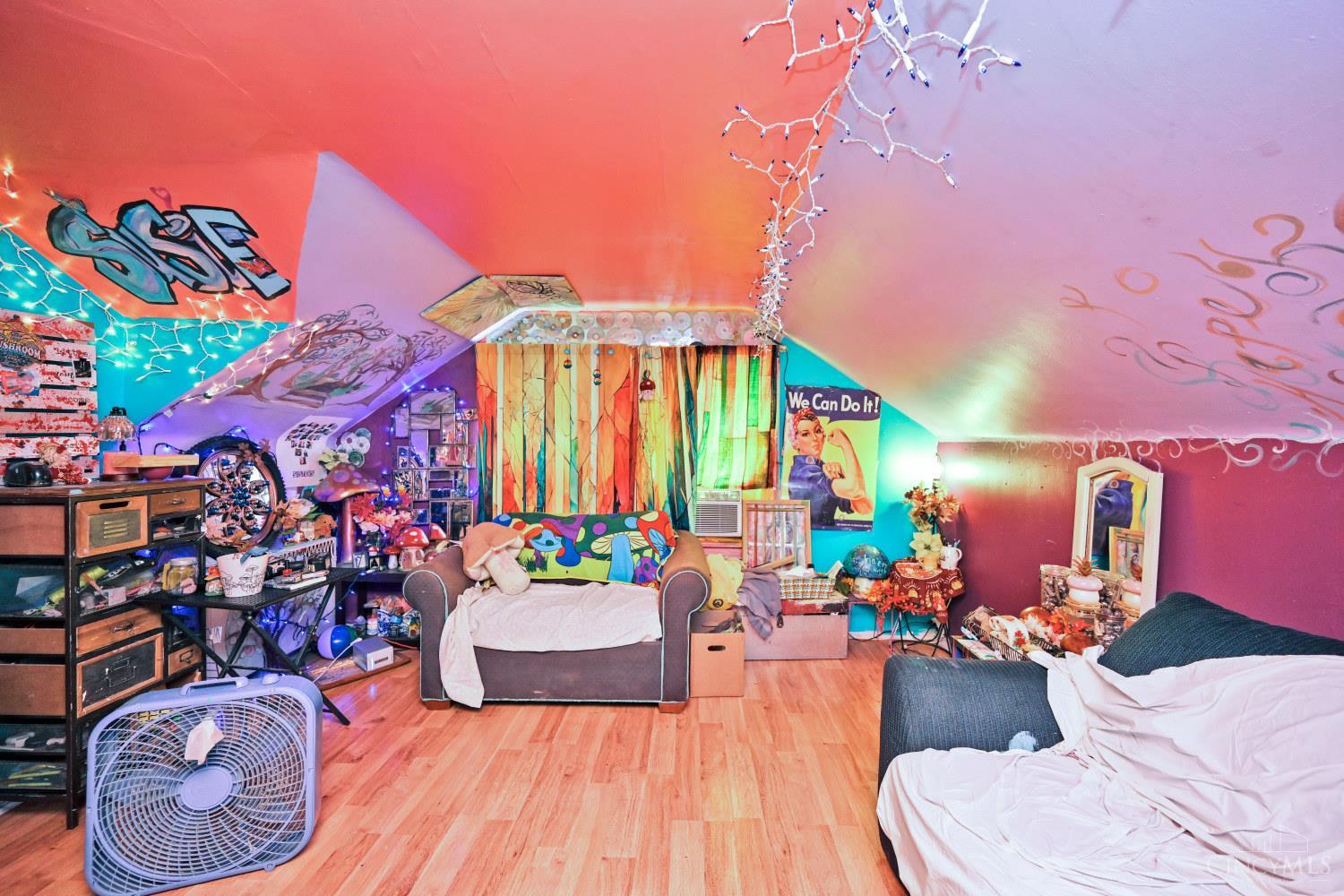 Colorfully decorated attic bedroom with a sloped graffiti-covered ceiling, string lights, and a sofa beside the bed.