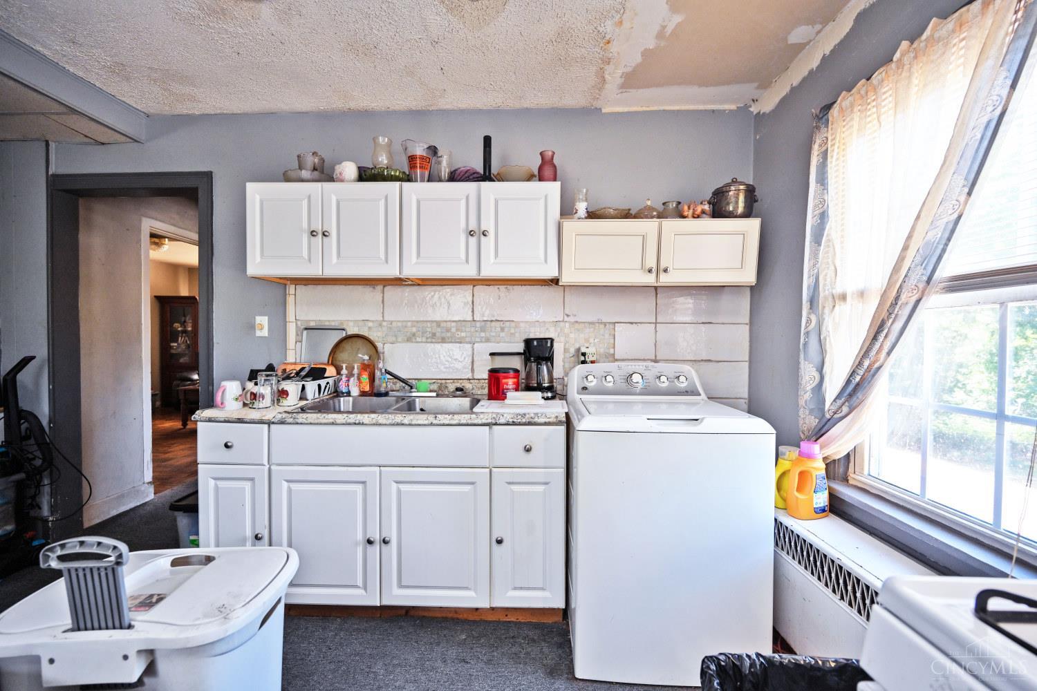 Kitchen with white cabinets, a sink, and a top-loading washing machine beside a large window.