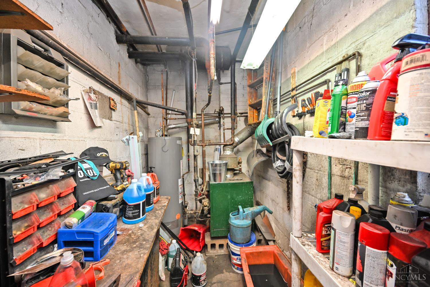 Crowded utility room with exposed pipes, a water heater, and shelves of tools and supplies.