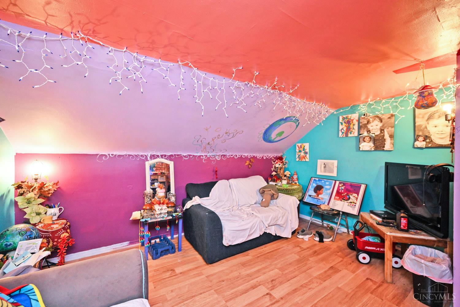 Colorfully painted attic bonus room with a sloped ceiling, string lights, sofa, television, and toys.