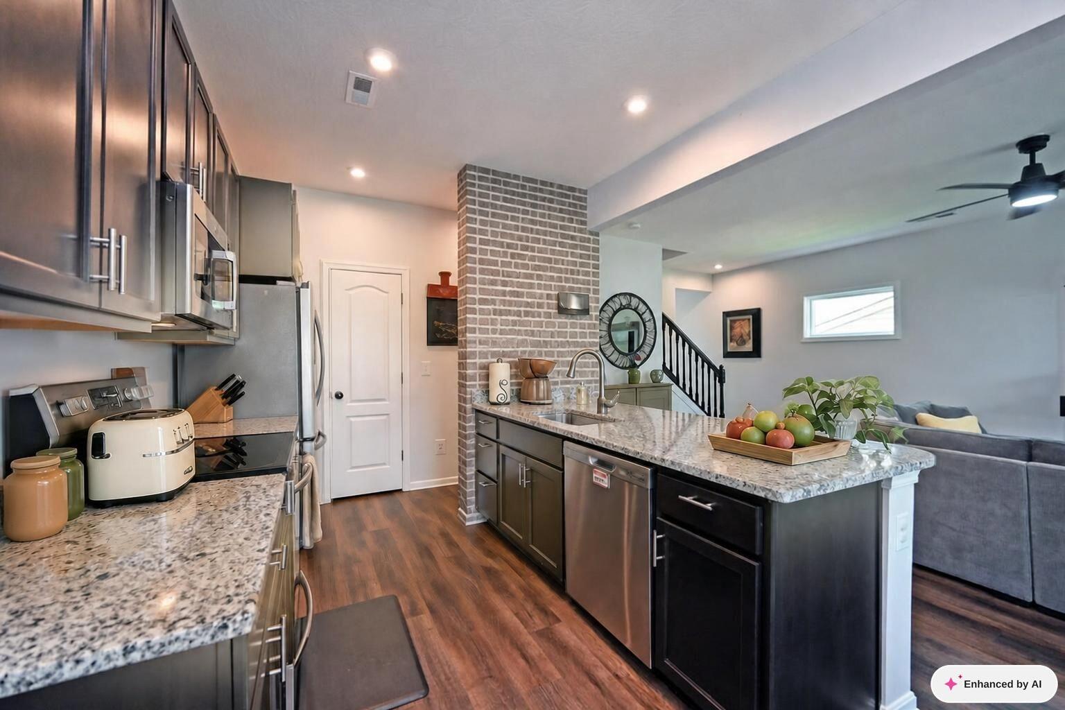 Open kitchen with a granite island, dark cabinets, stainless appliances, and a brick accent wall.