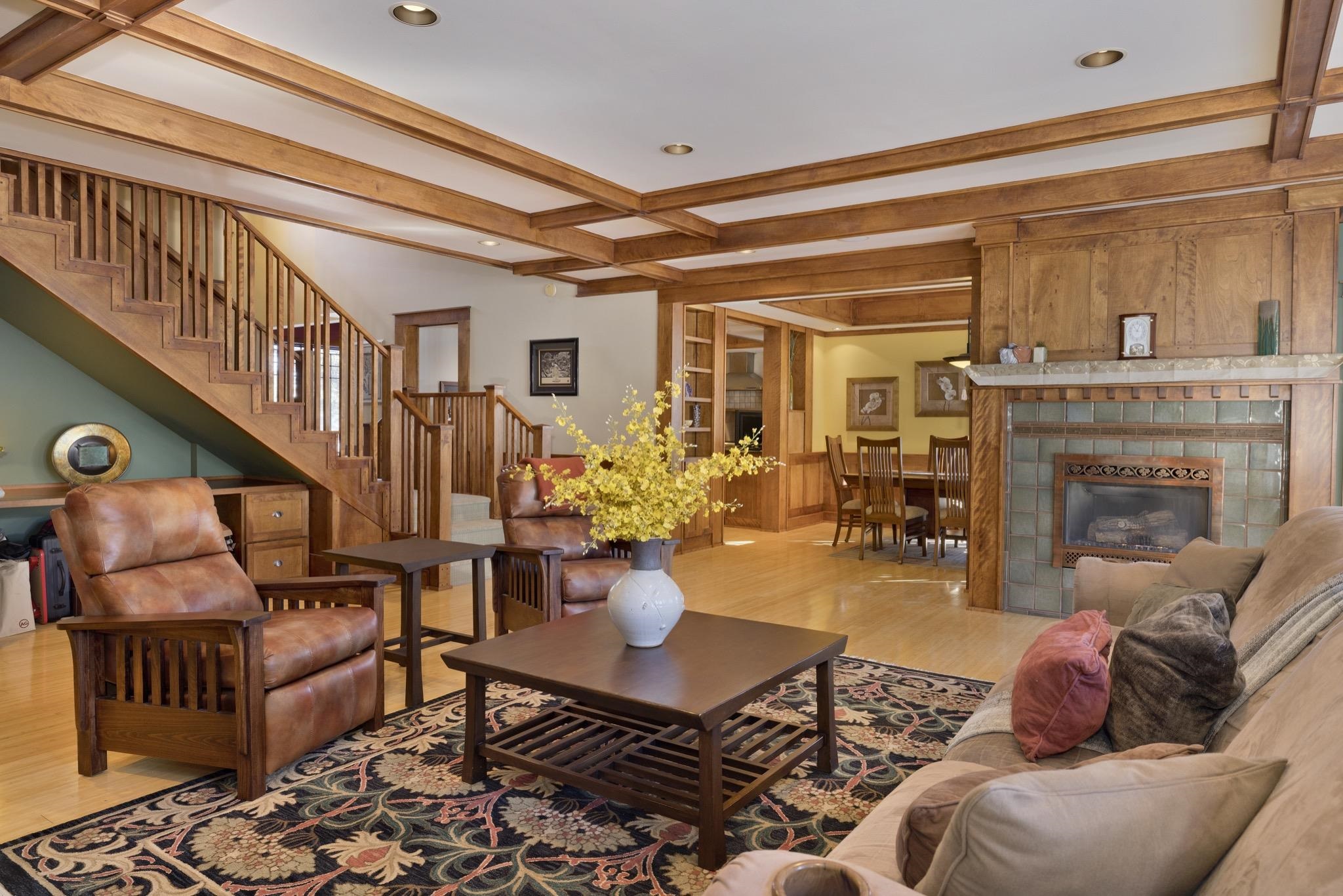 Living room with a tiled fireplace, wood staircase, and exposed ceiling beams.