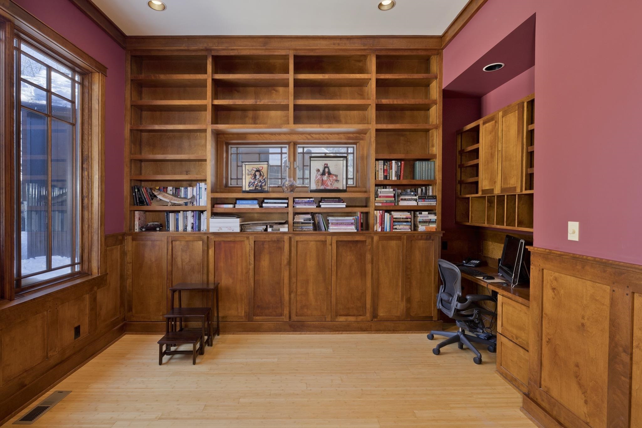 Home office with built-in wooden bookshelves, a desk, and a large window.