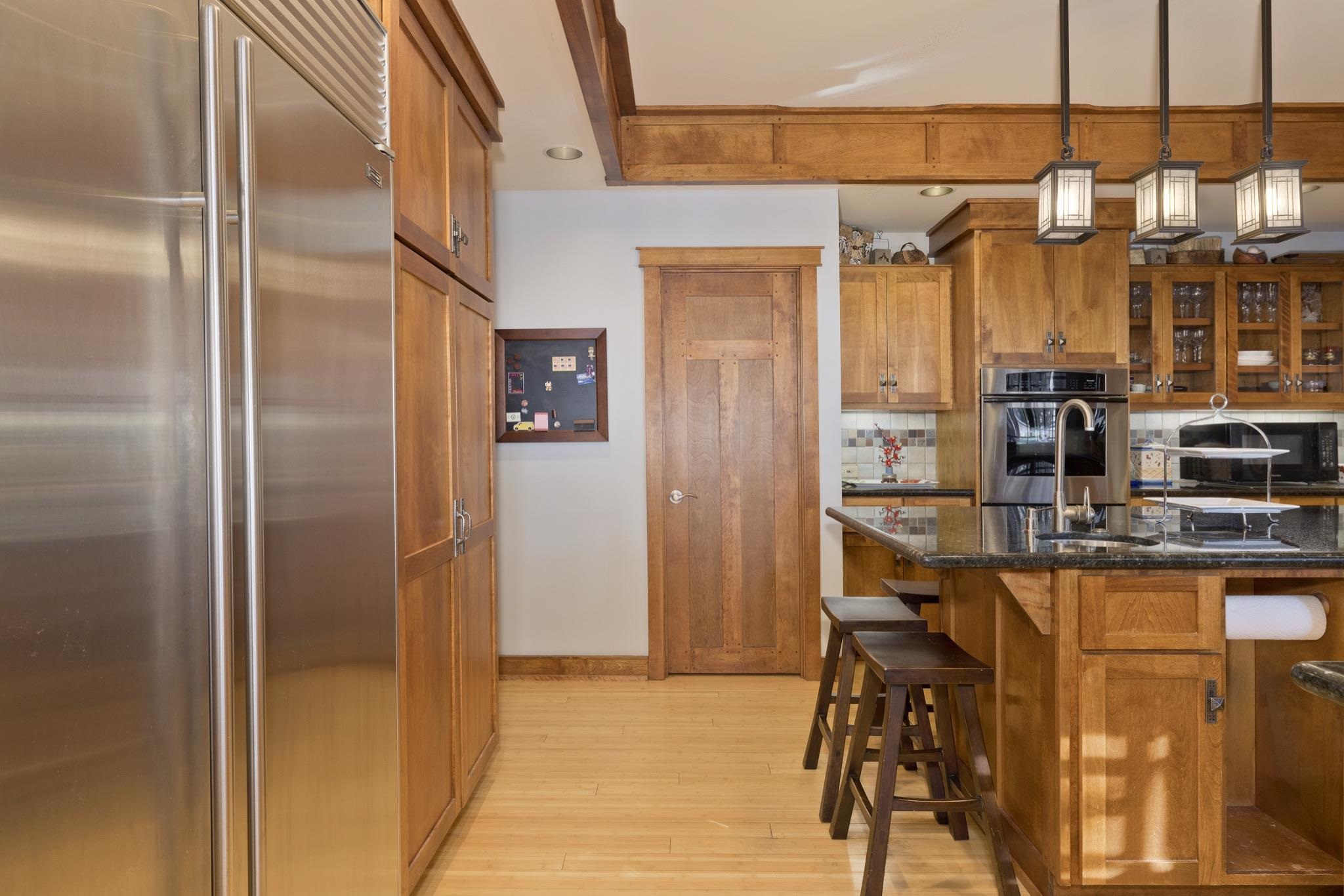 Kitchen with wood cabinetry, stainless steel appliances, and a granite island with bar stools.