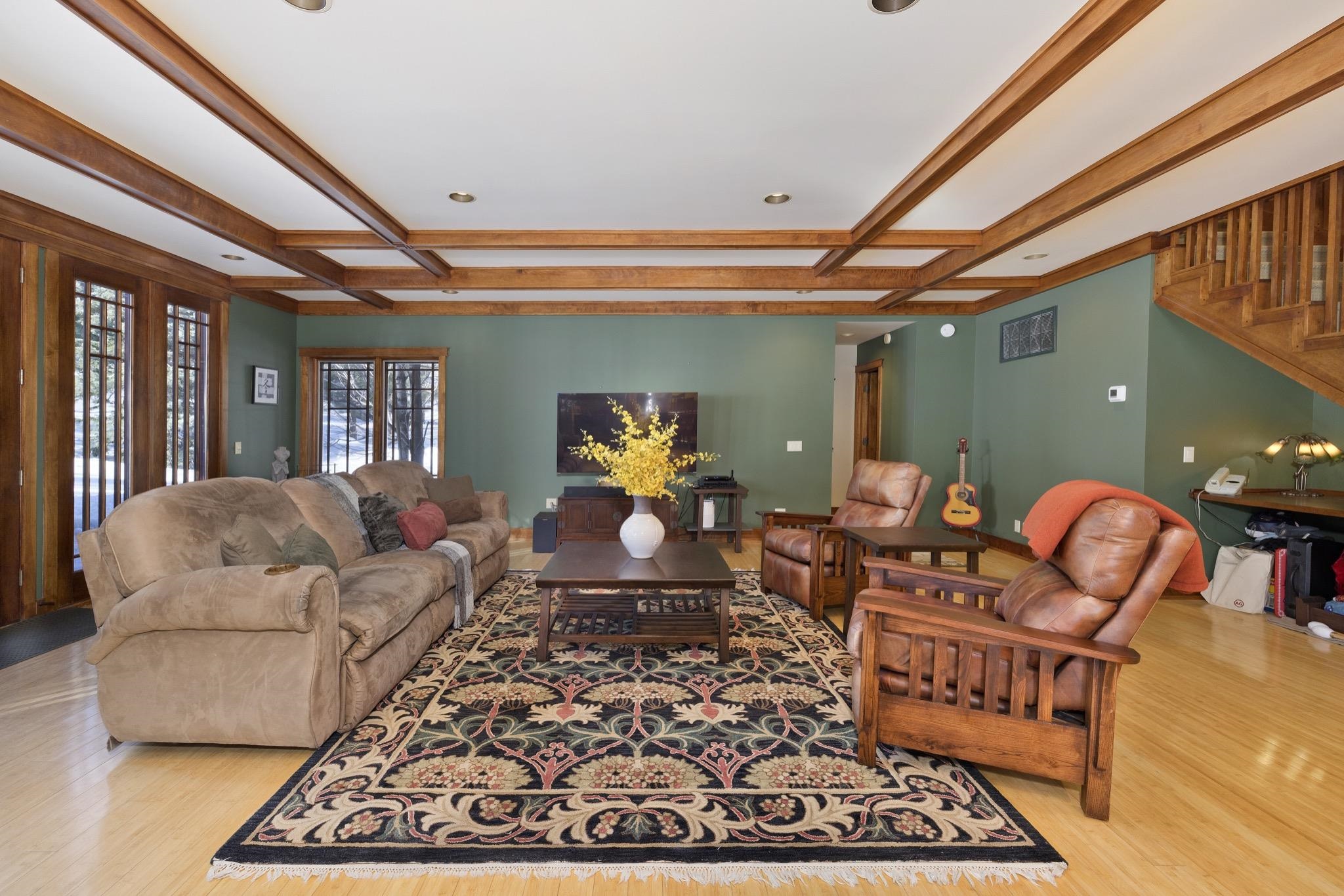Living room with exposed wood ceiling beams, a patterned rug, leather armchairs, and snowy views through tall windows.