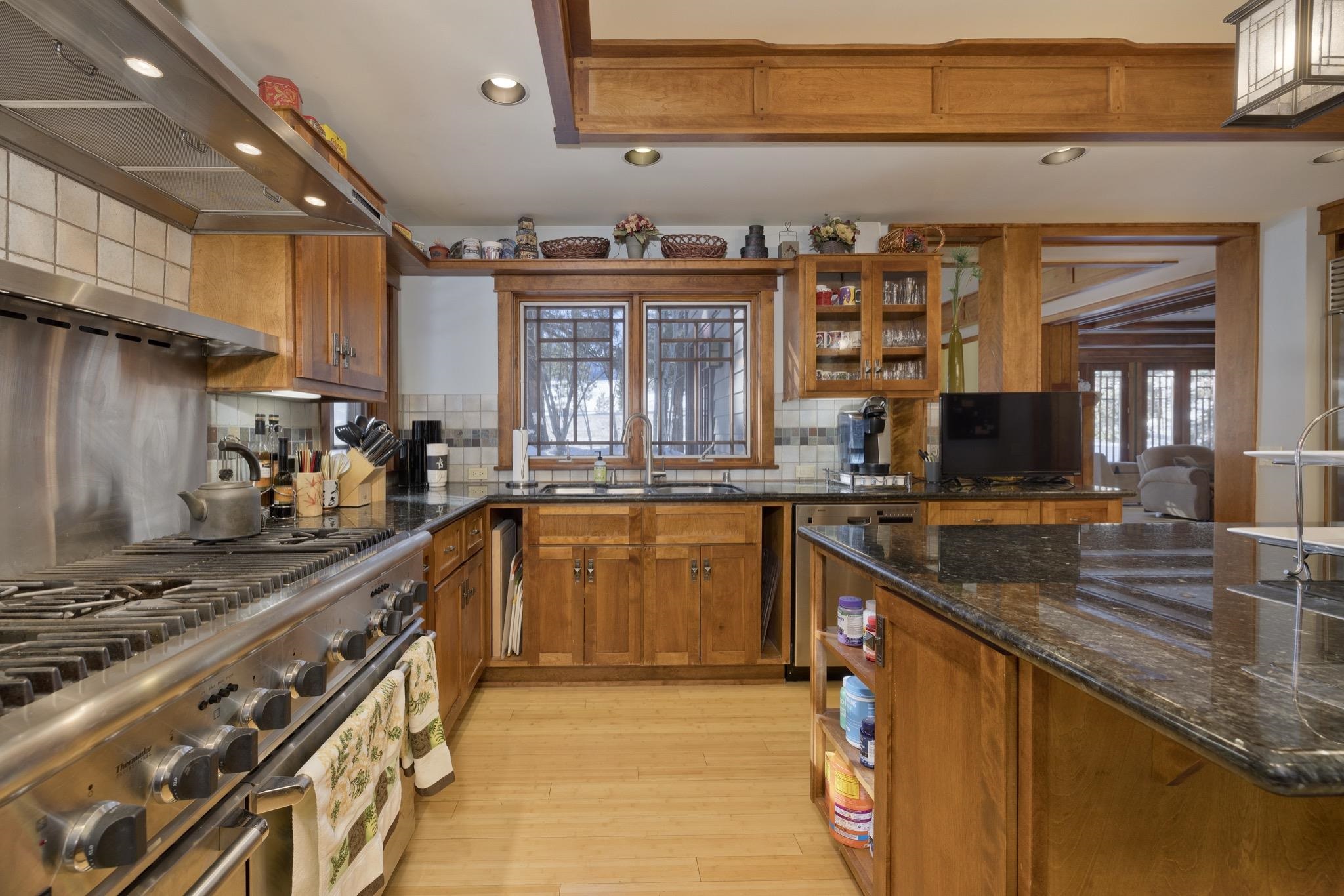 Kitchen with warm wood cabinetry, a large stainless-steel gas range, and a dark stone island.