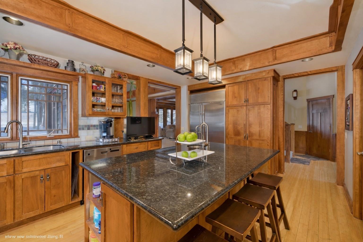 Wood-accented kitchen with a granite island, bar stools, stainless steel appliances, and pendant lights.