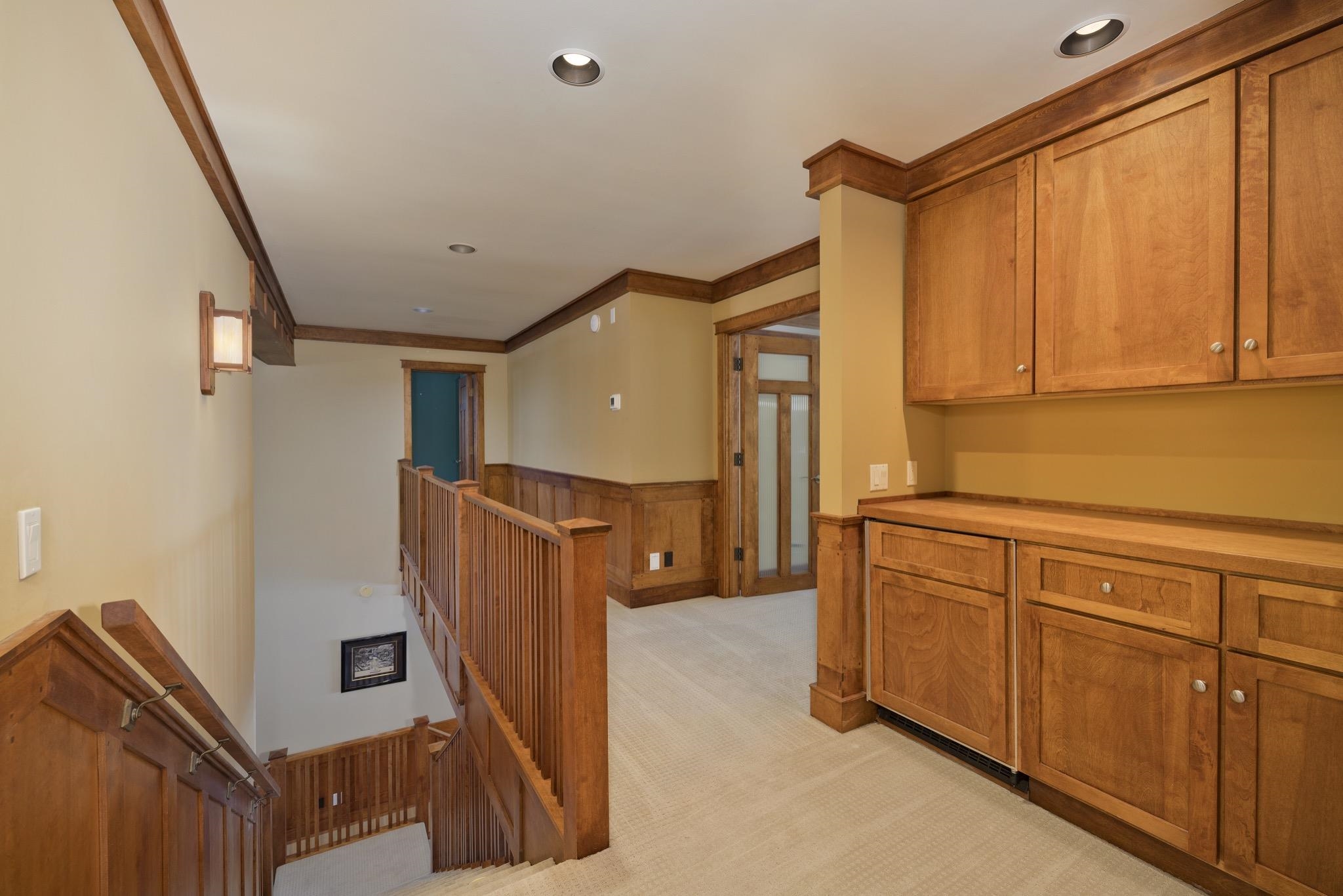 Carpeted hallway landing with a wooden staircase, railing, and built-in cabinets.