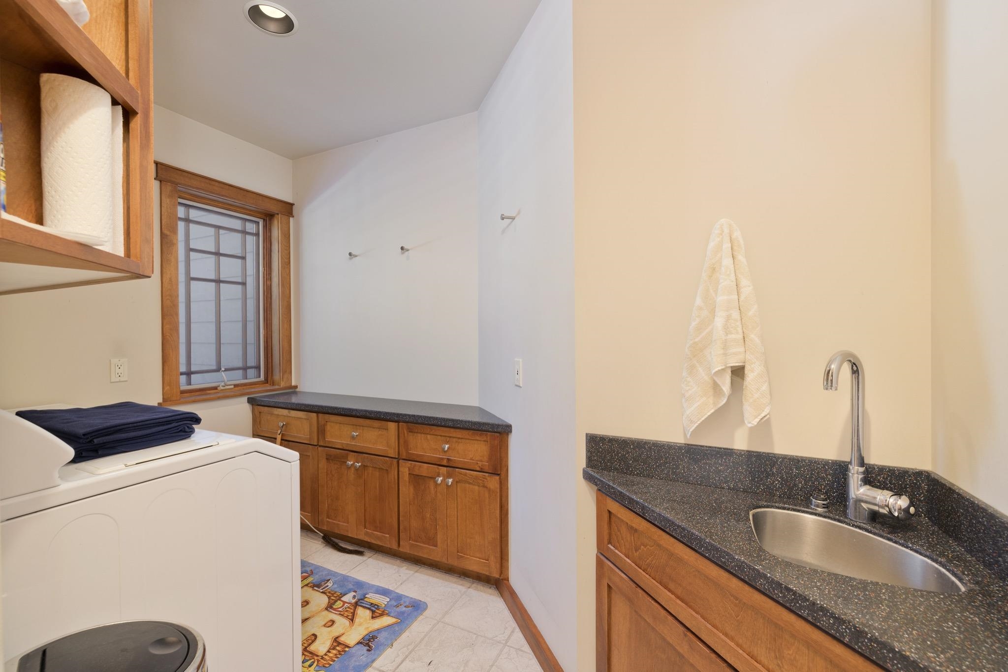 Laundry room with a washer and dryer, utility sink, dark countertops, and warm wood cabinetry.