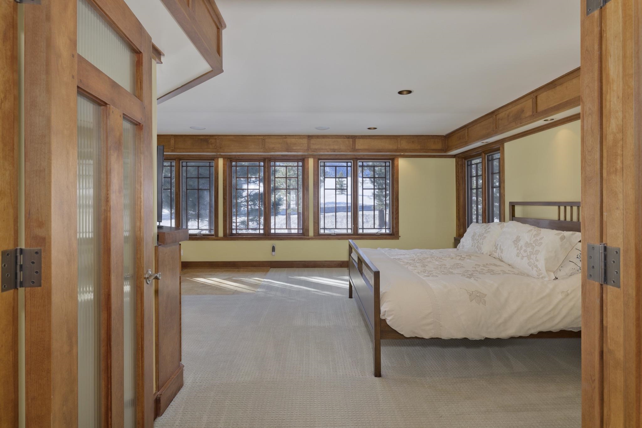 Bedroom with a wood-framed bed and broad windows overlooking snowy ground and trees.