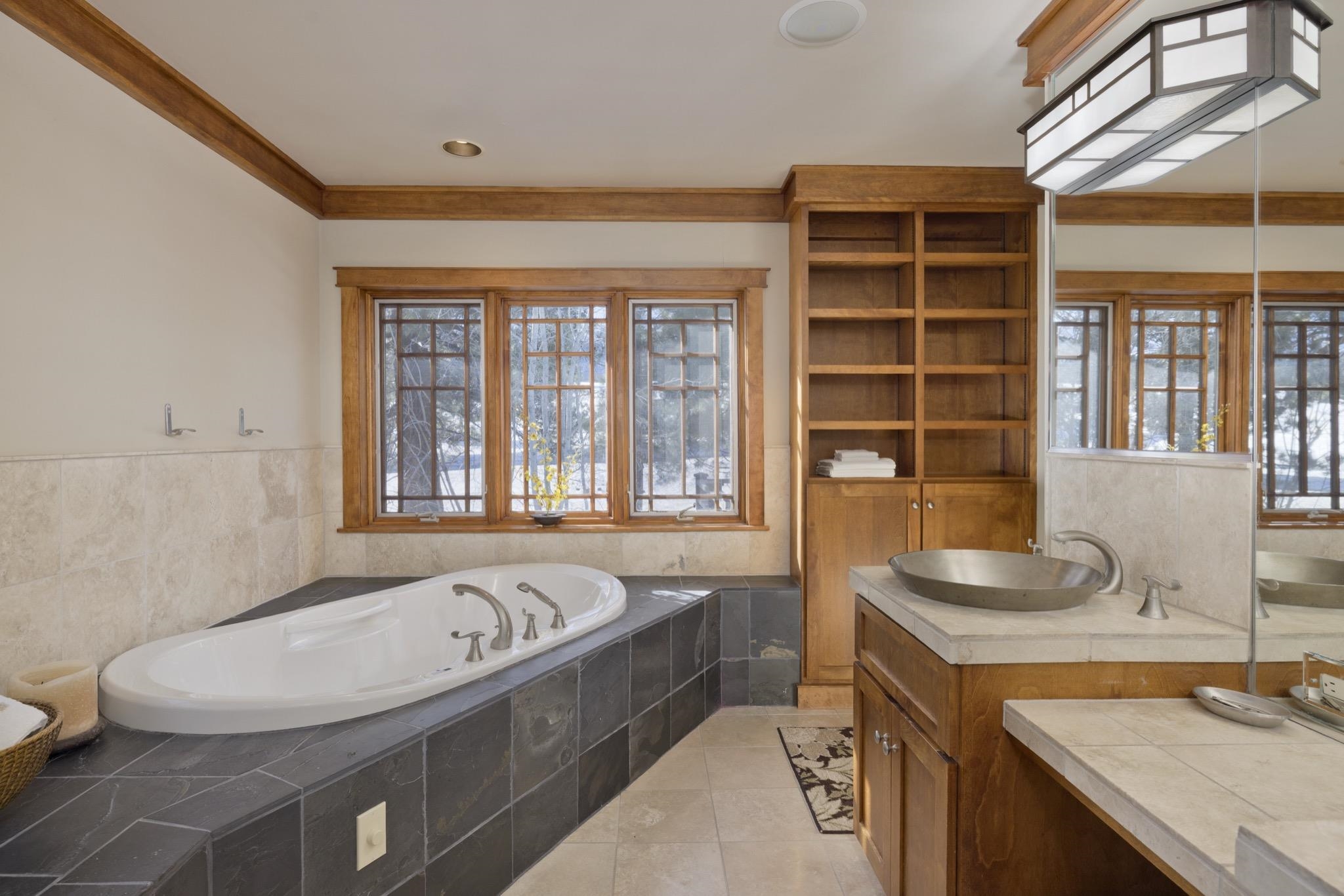 Bathroom with a corner soaking tub, vessel sink, built-in shelving, and snowy views through large windows.