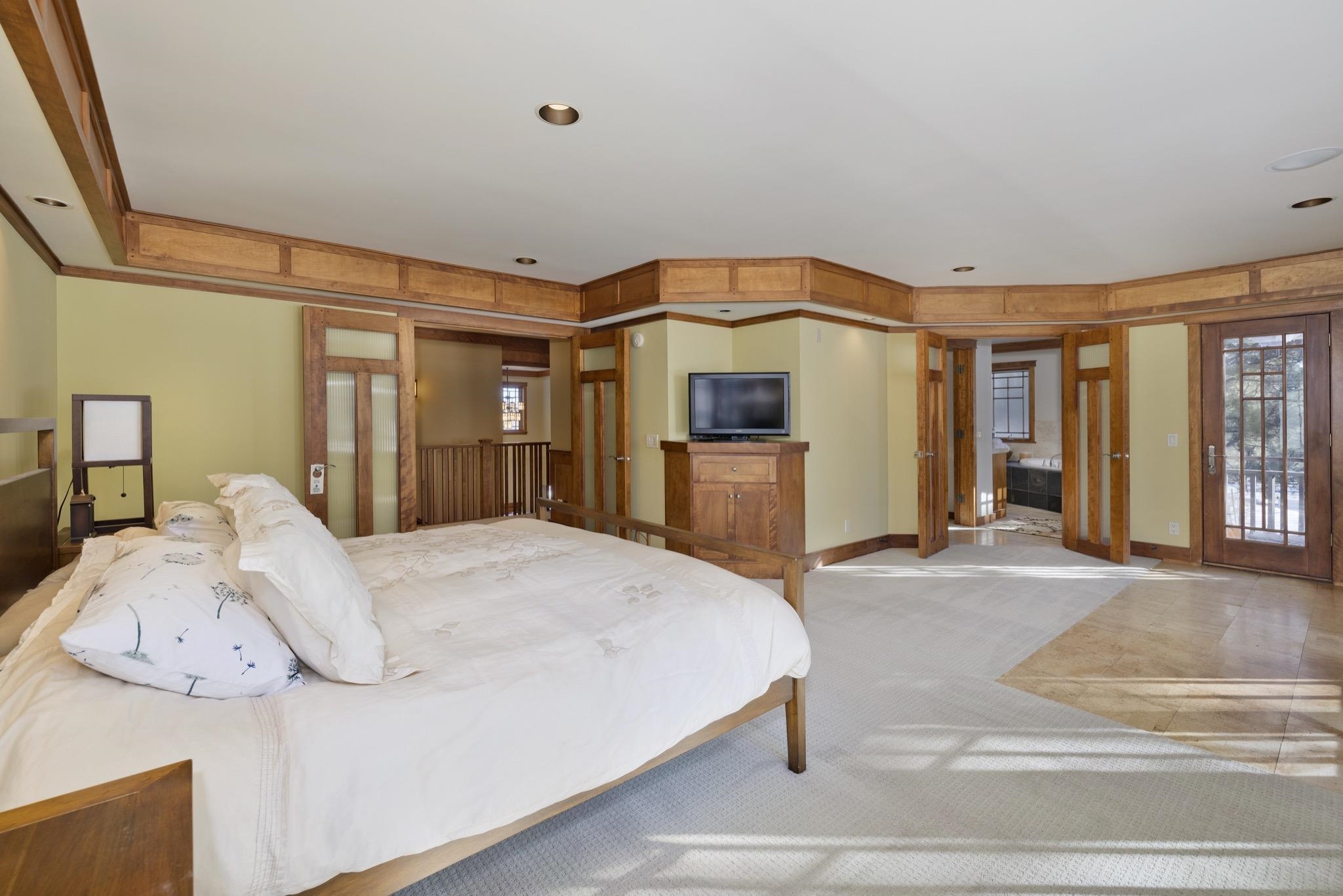 Bedroom with a large white bed, warm wood trim, and a television on a wooden cabinet.
