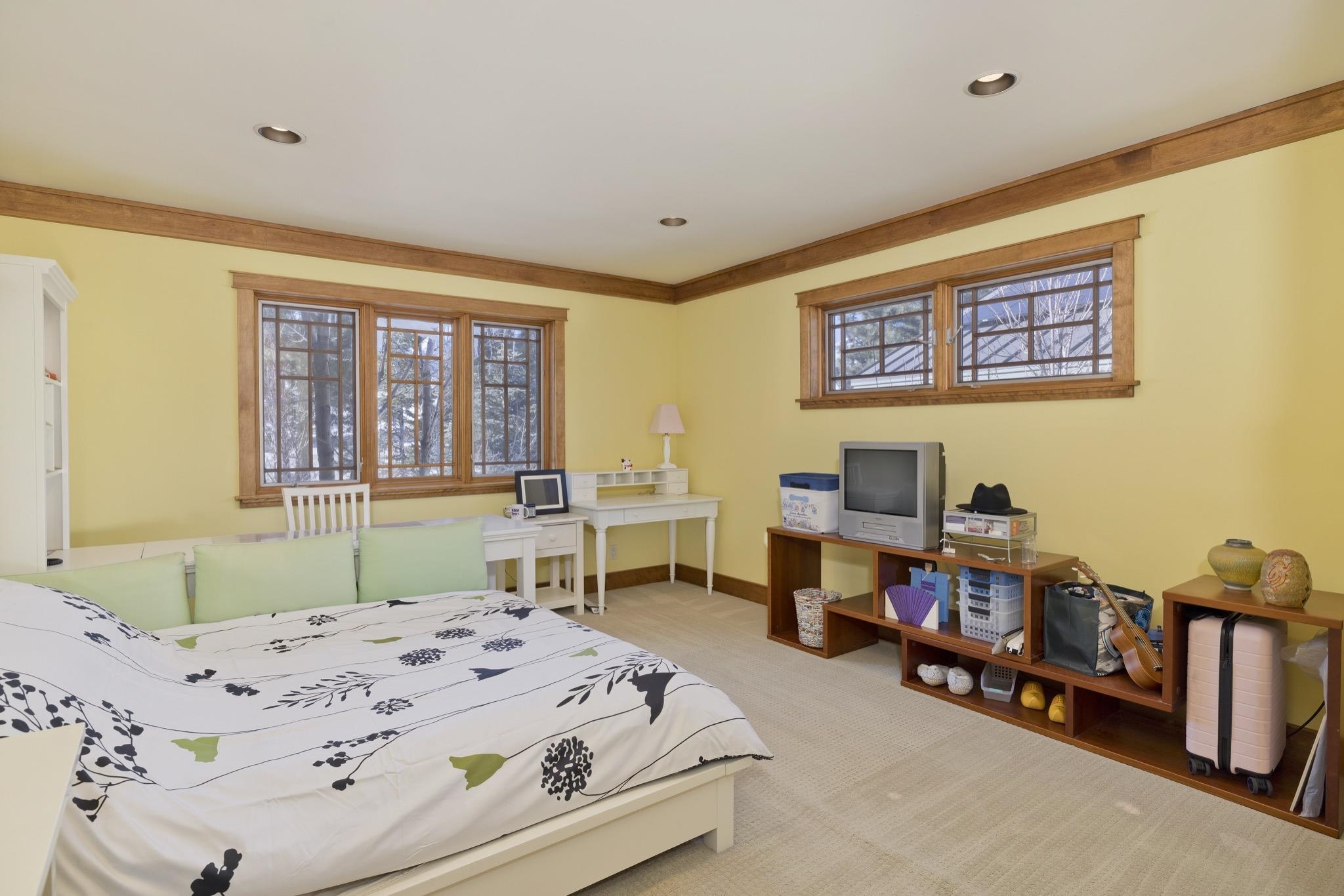 Bedroom with floral bedding, yellow walls, wood-trimmed windows, and a desk.