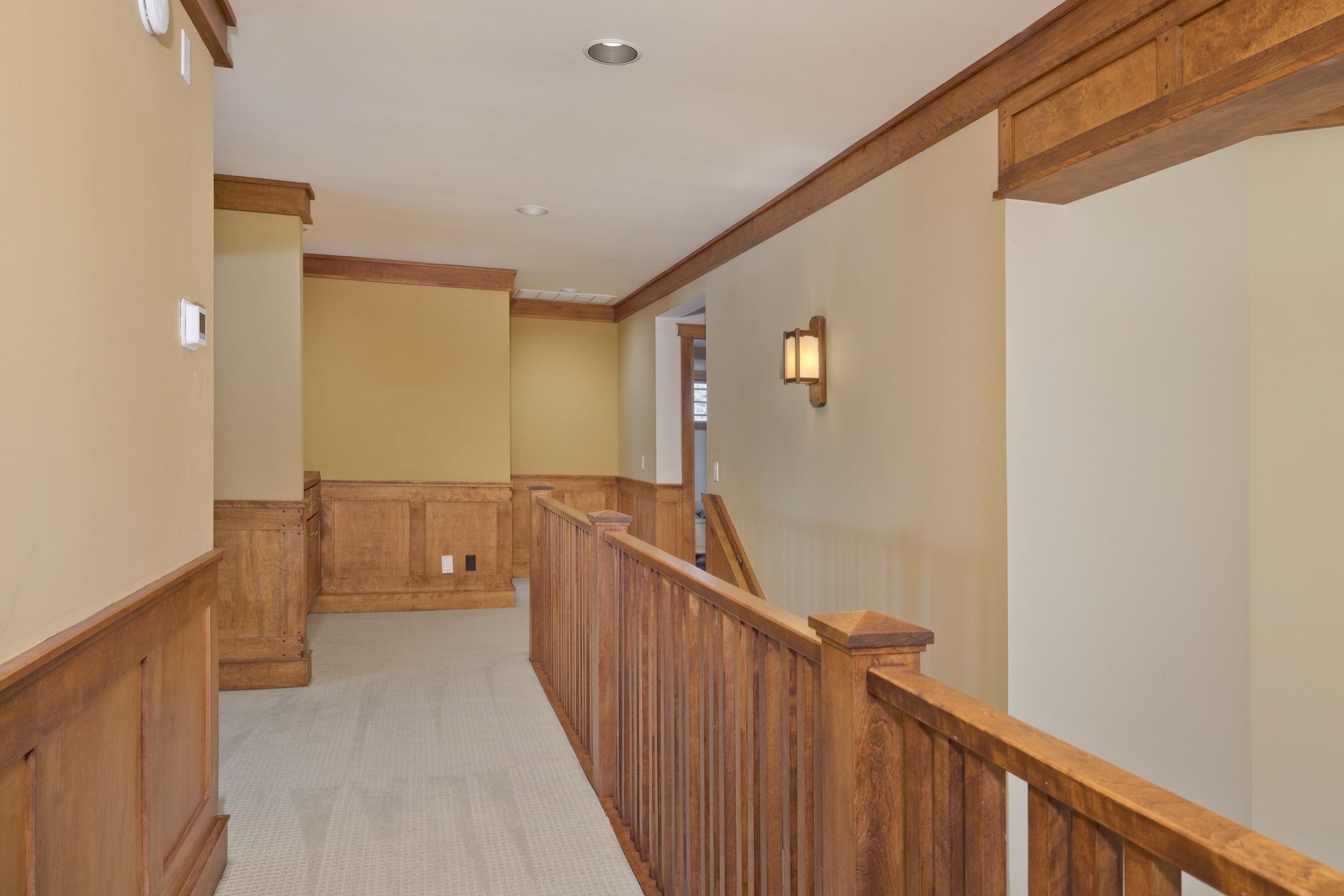 Empty upstairs hallway with carpet, wood paneling, and a wooden stair railing.