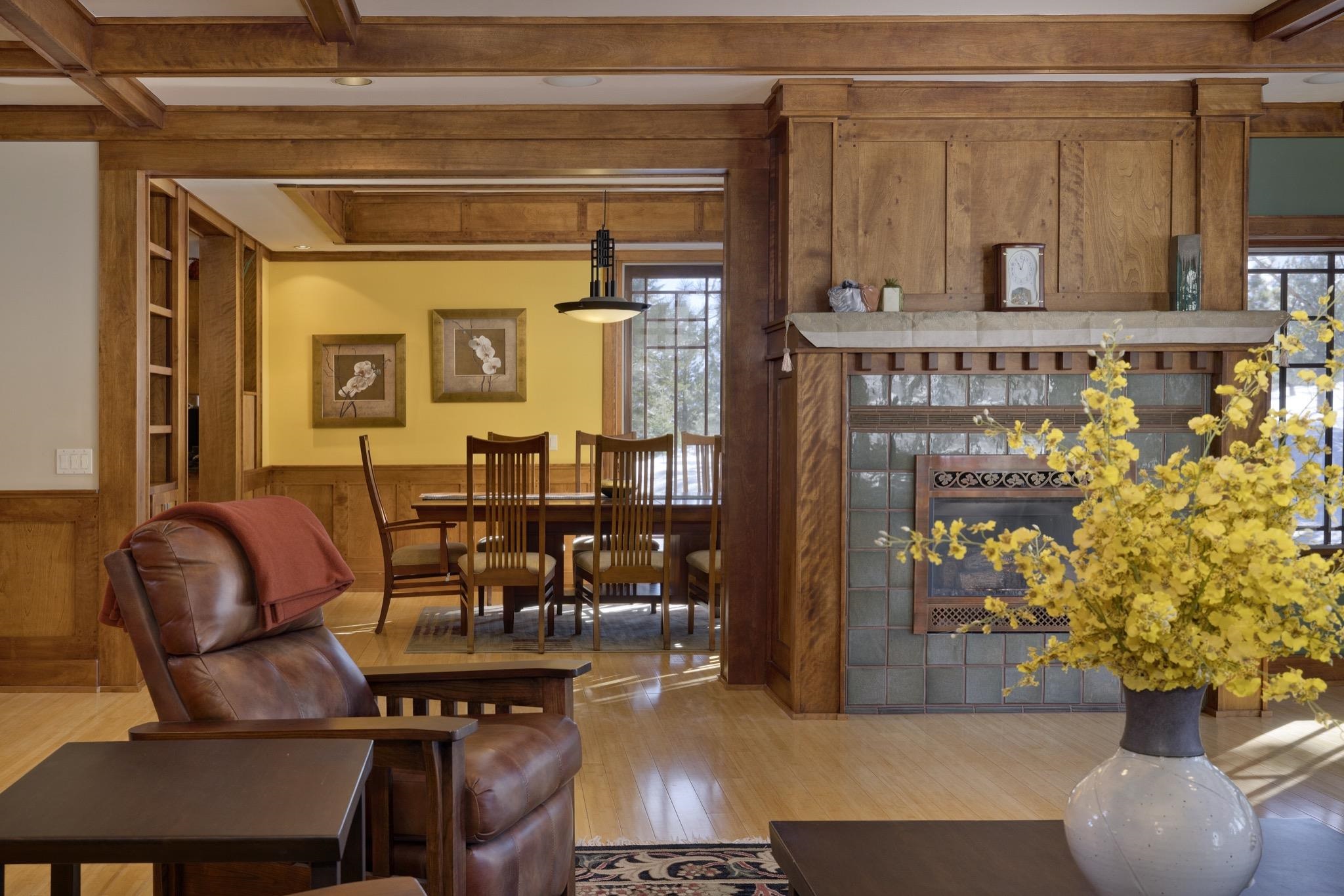 Wood-paneled living room with a tiled fireplace, leather recliner, and dining area beyond.
