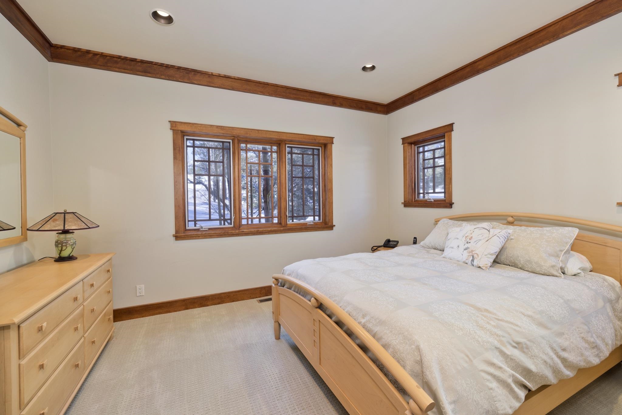 Bedroom with a light wood bed and dresser, wood-trimmed windows, and snowy trees outside.