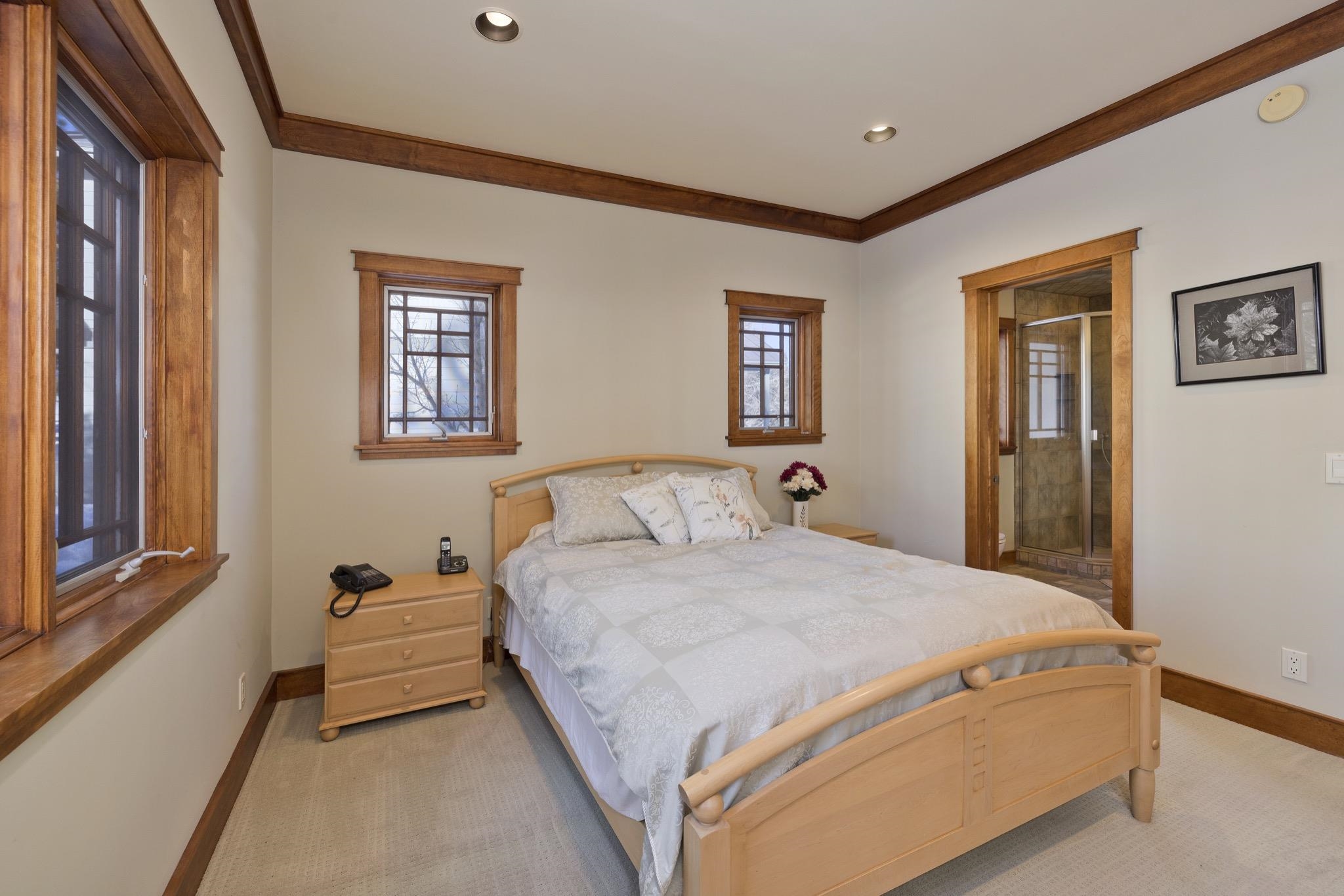 Bedroom with a light wood bed, matching wood window trim, and an ensuite glass shower.