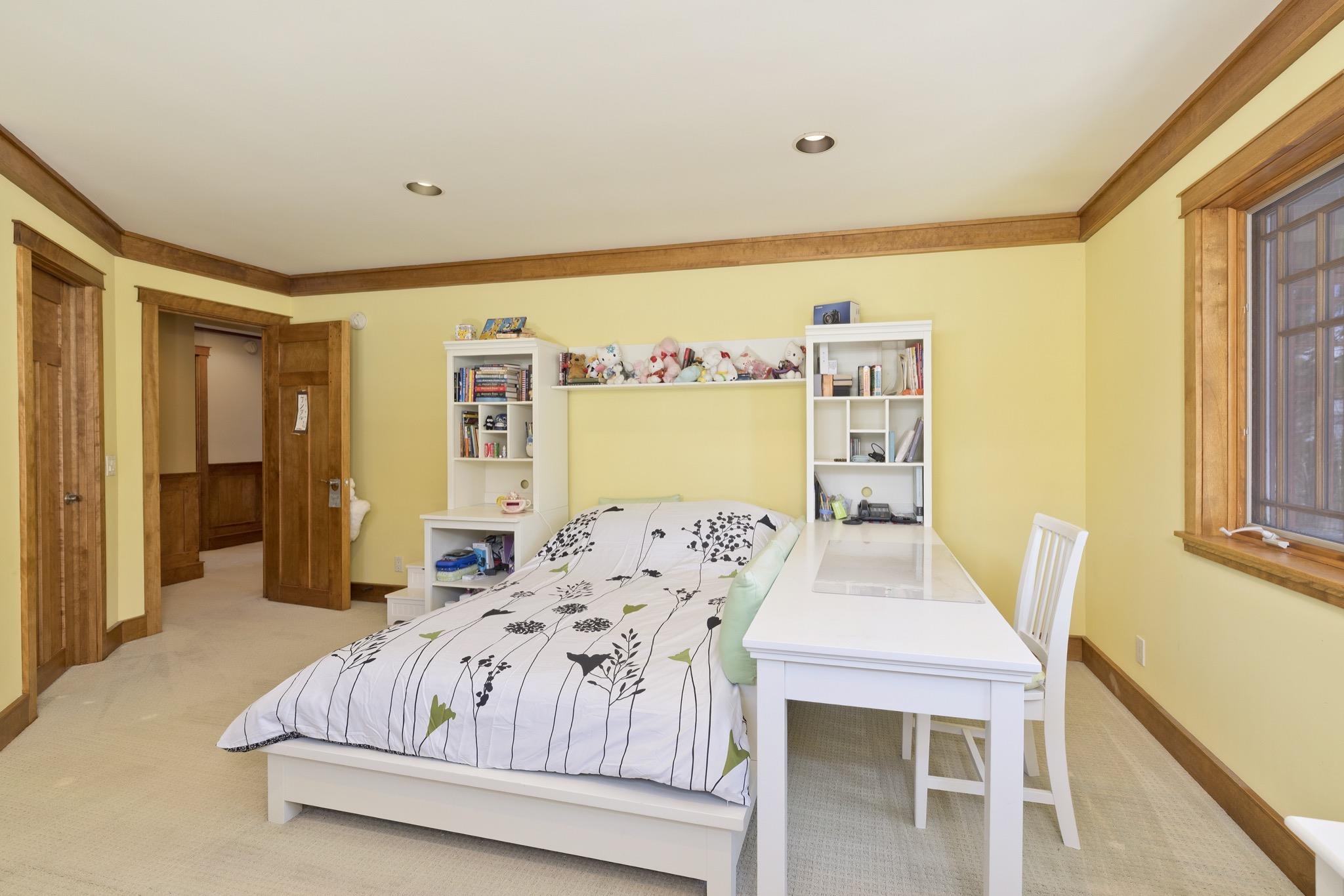 Bedroom with botanical-print bedding, a white desk, and bookshelves beneath pale yellow walls.