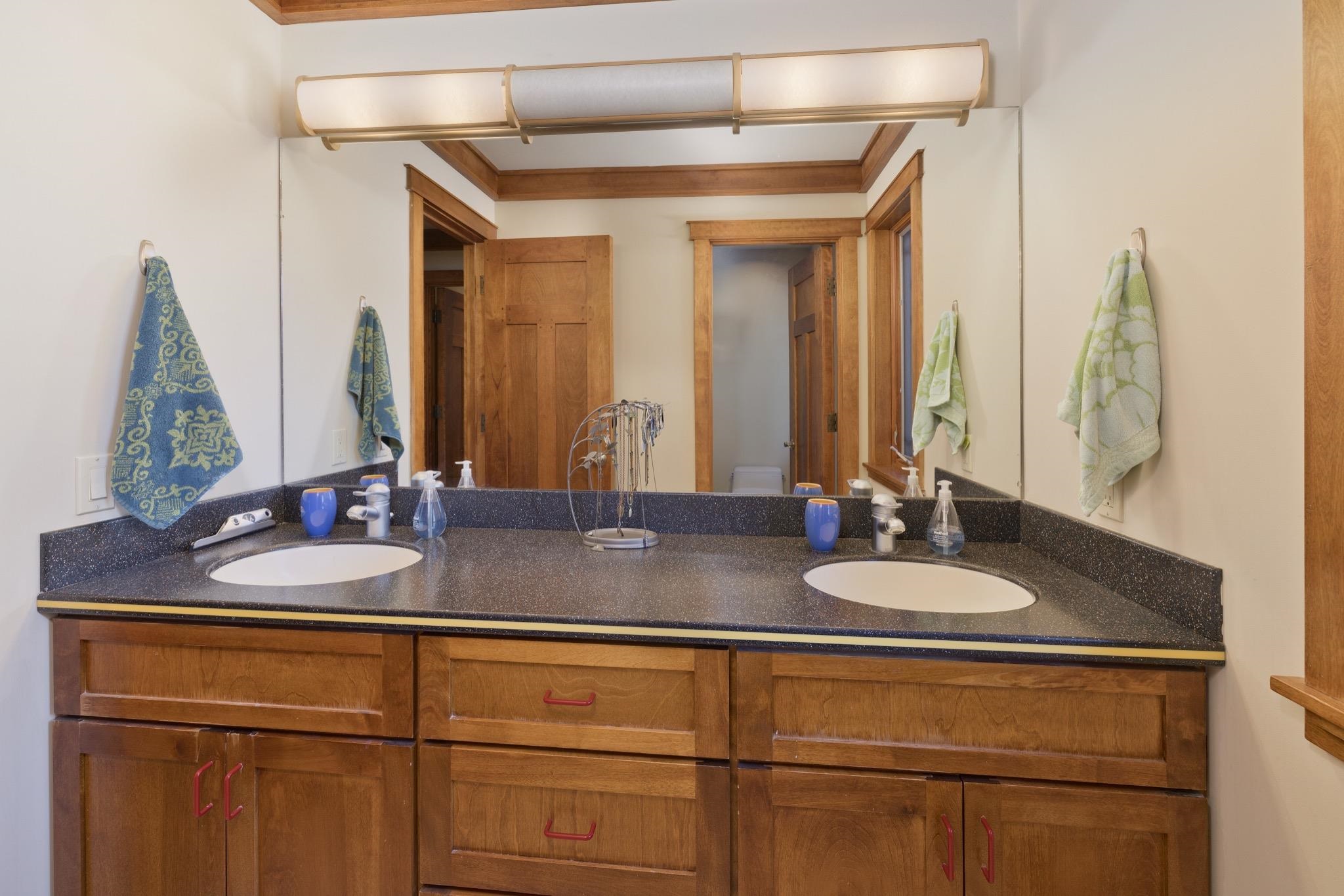 Bathroom vanity with two sinks, a wide mirror, and warm wood cabinetry.