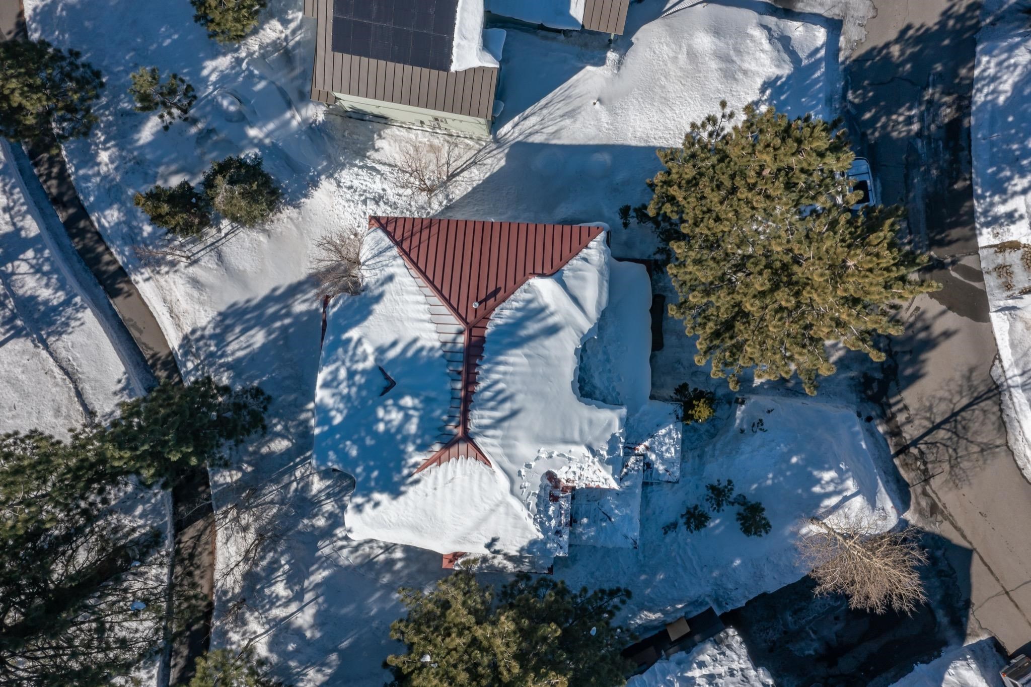 Snow-covered home with a red metal roof, surrounded by pine trees.