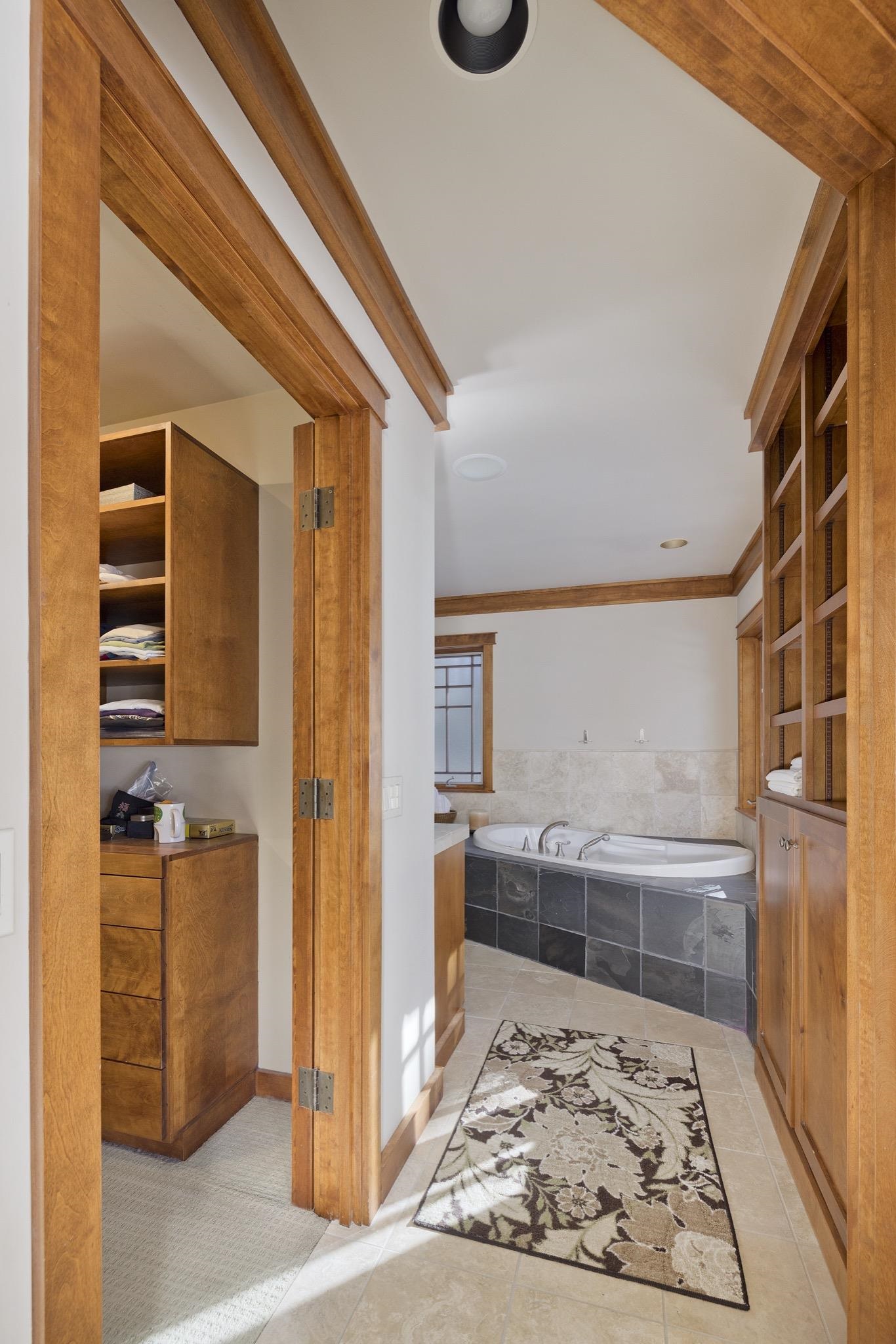 Bathroom with a built-in soaking tub, dark tile surround, and warm wood cabinetry.